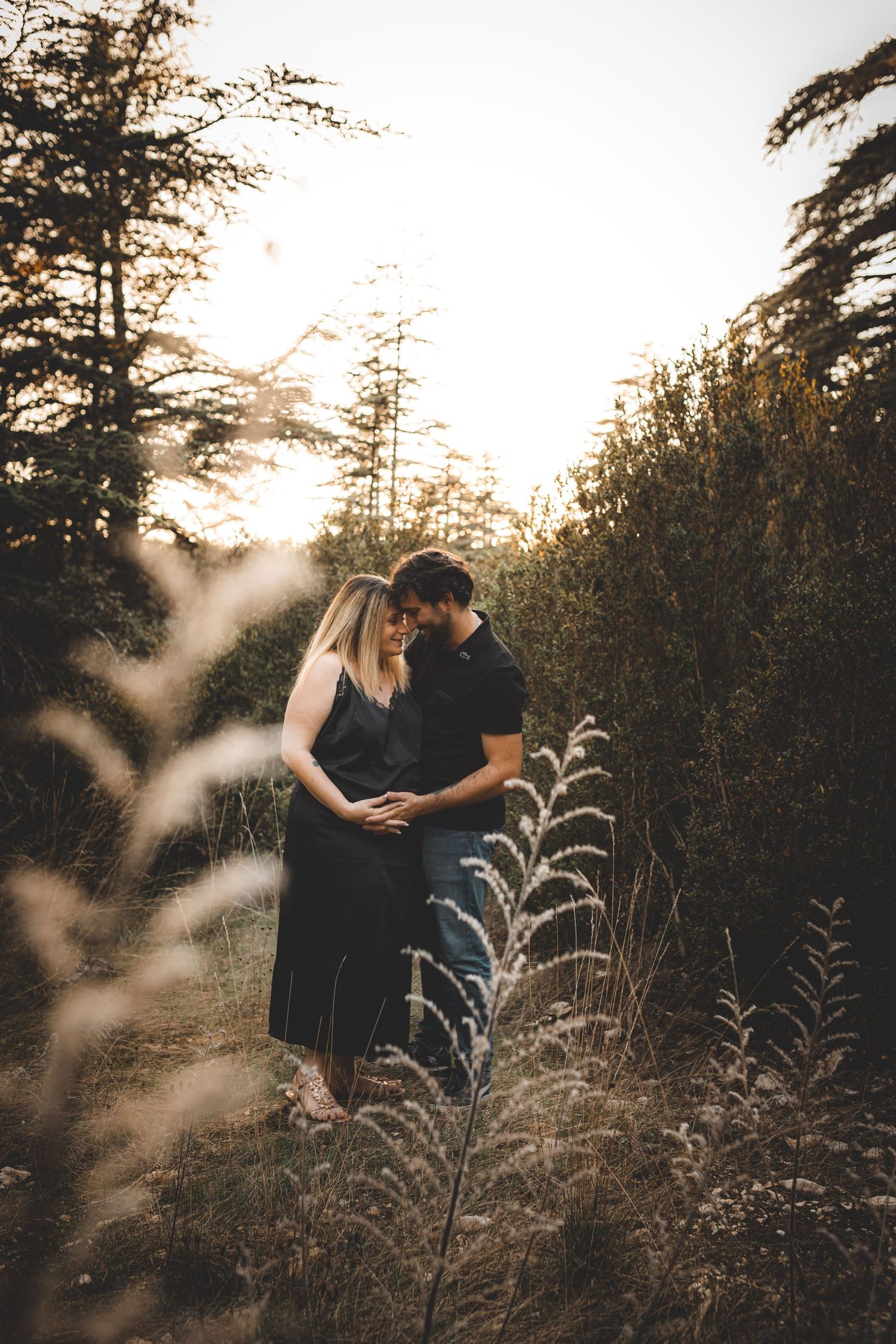Couple avec une femme enceinte qui s'enlace face à face dans un écrin de verdure à la forêt des cèdres dans le Luberon à Bonnieux