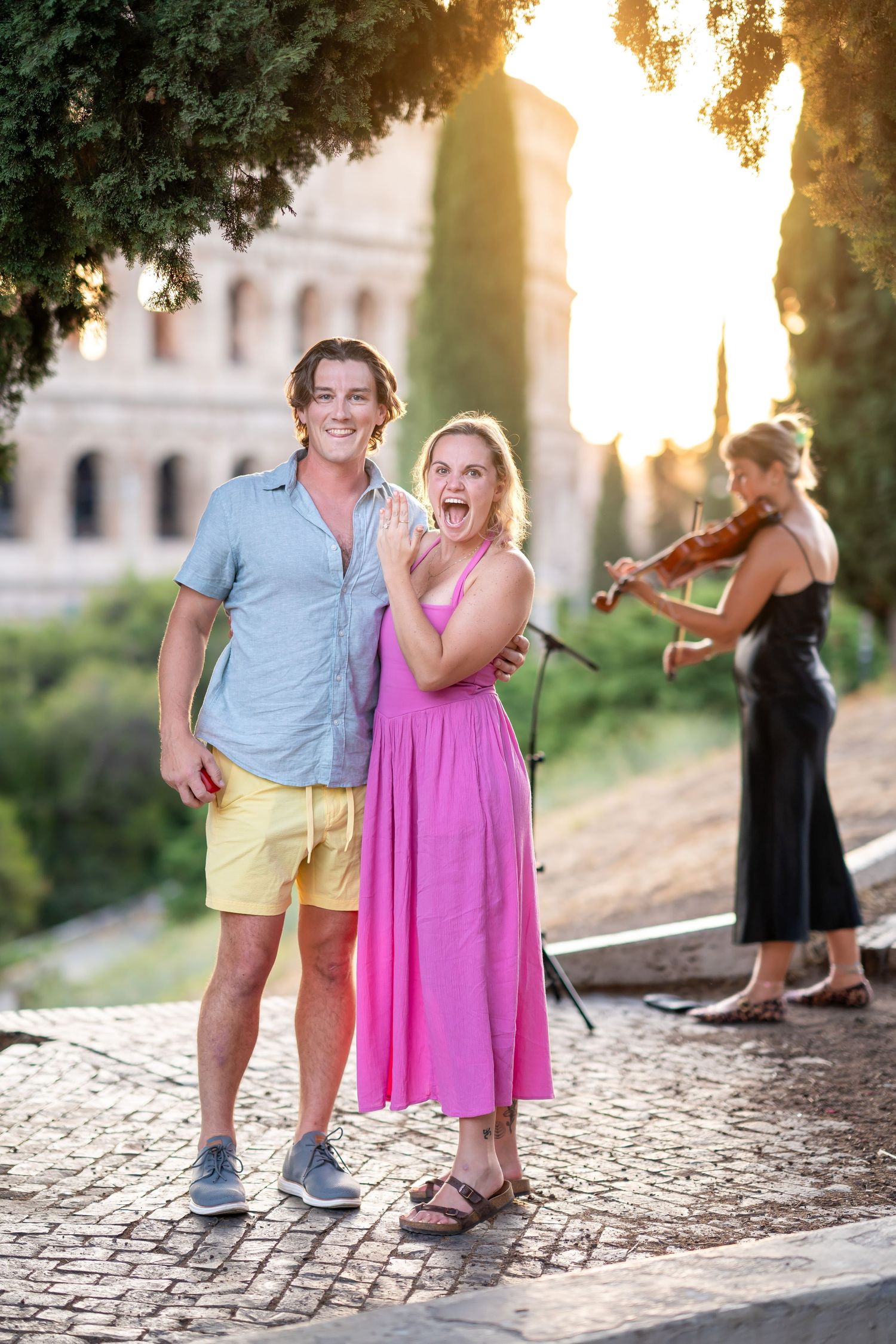 Couple posing happily in Rome with a violinist and the Colosseum at sunset in the background.