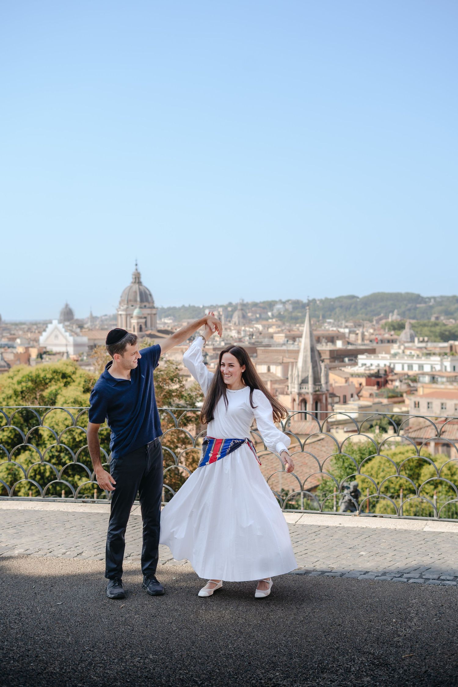 A couple dancing on a rooftop terrace with the Rome cityscape and domed church in the background.
