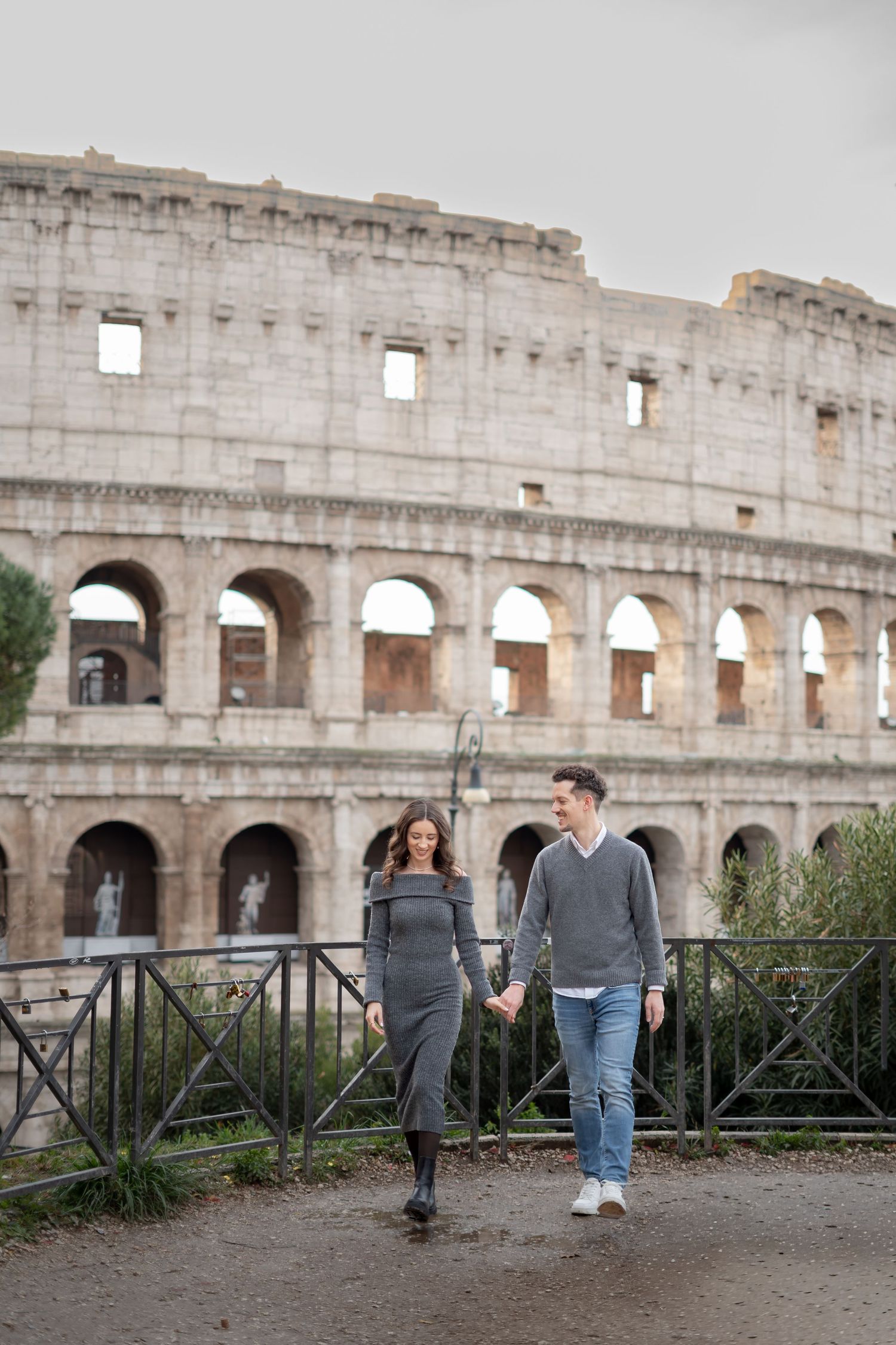 Couple holding hands and walking in front of the Colosseum in Rome, Italy.