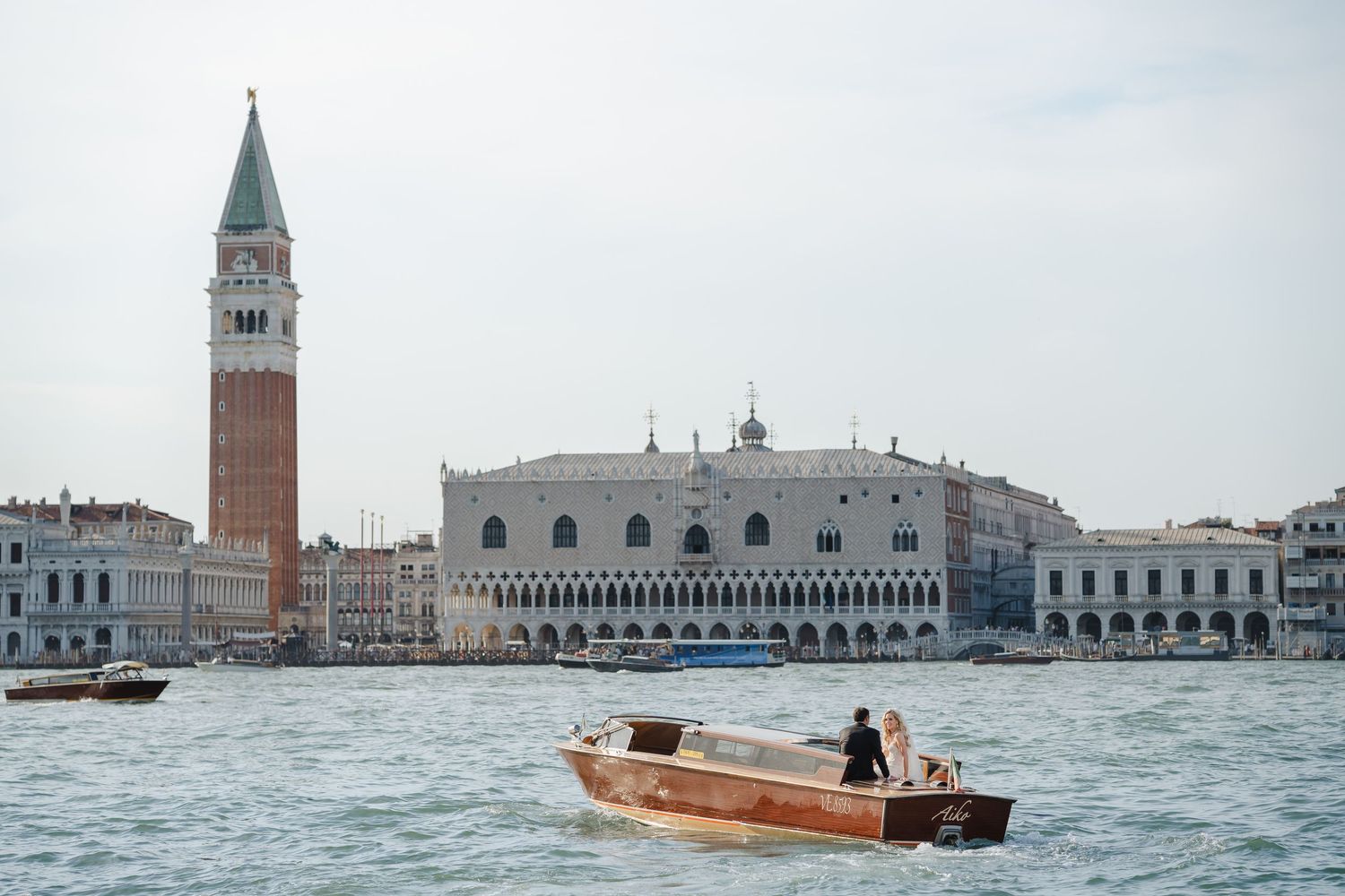 Classic wooden boat gliding past Venice's Doge's Palace and St. Mark's Campanile on the lagoon.