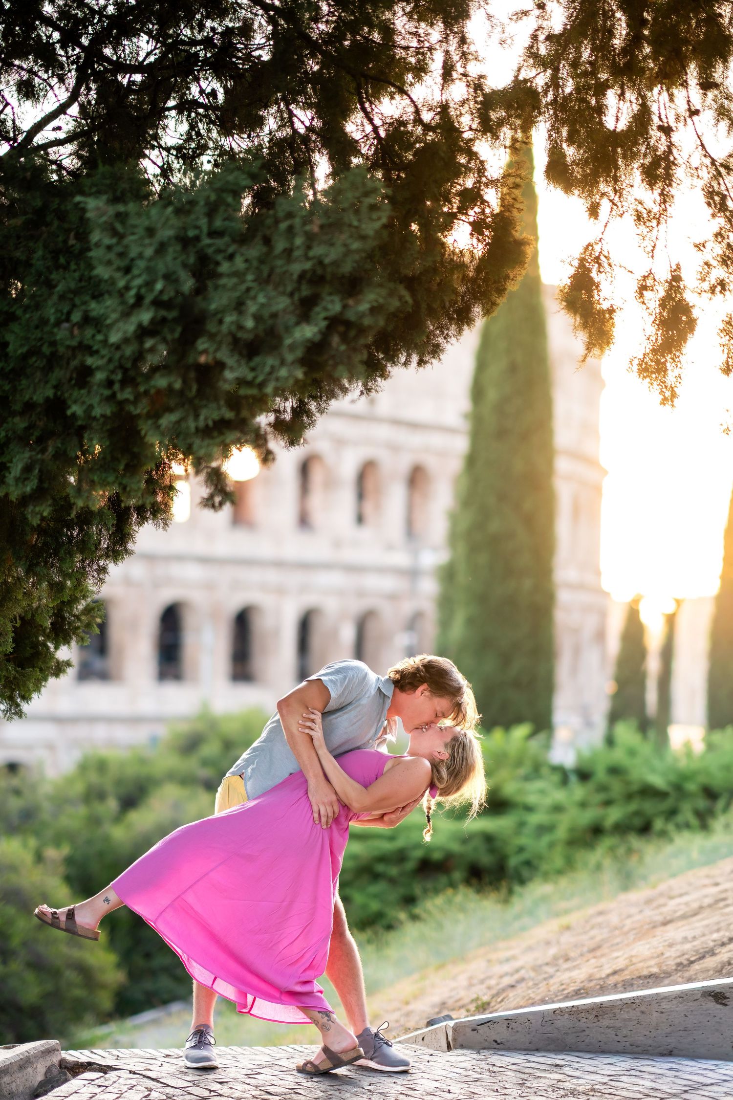 Romantic couple sharing a dip kiss at sunset with the Colosseum in Rome, Italy in the background.