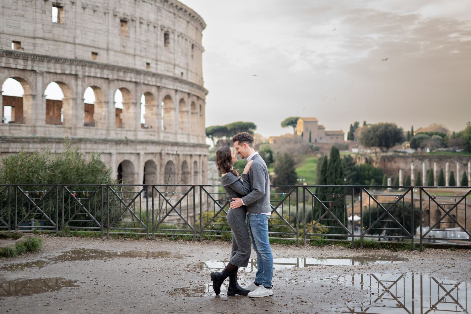 Couple embracing romantically in front of the ancient Colosseum in Rome, Italy, on a cloudy day.