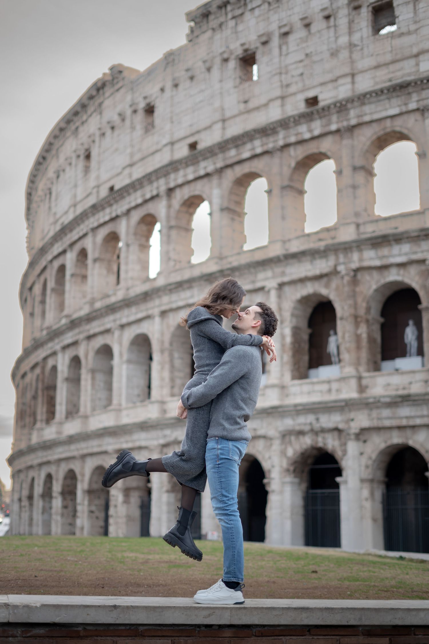 Romantic couple embracing in front of the Colosseum in Rome, Italy, on a cloudy day.