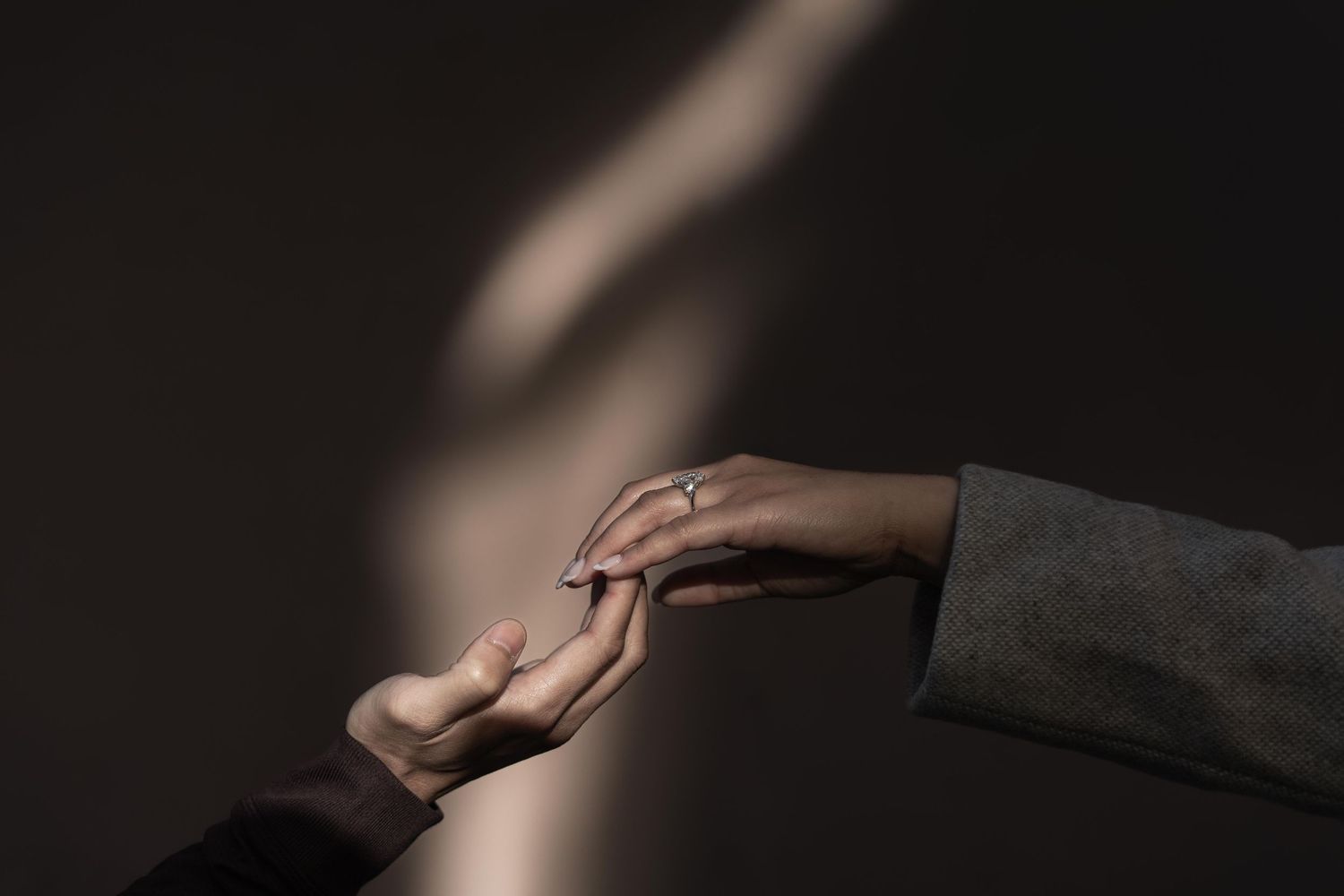Two hands gently reaching toward each other against a dark background with soft light, symbolizing connection.