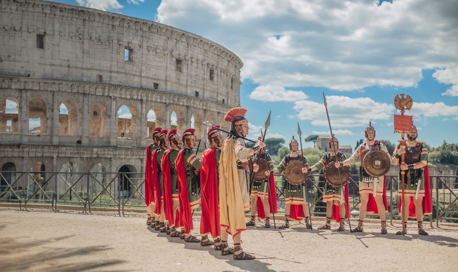 Roman gladiators marching in costume near the Colosseum in Rome, Italy under a blue sky.