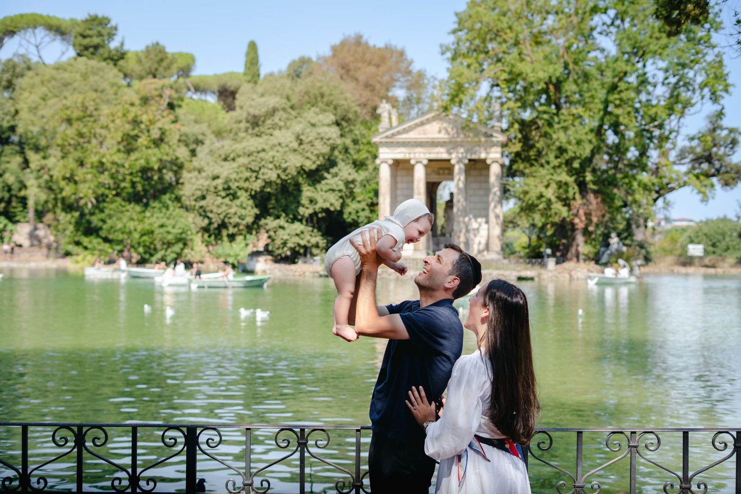 Family with baby at Villa Borghese lake, Rome, with Temple of Aesculapius in background.
