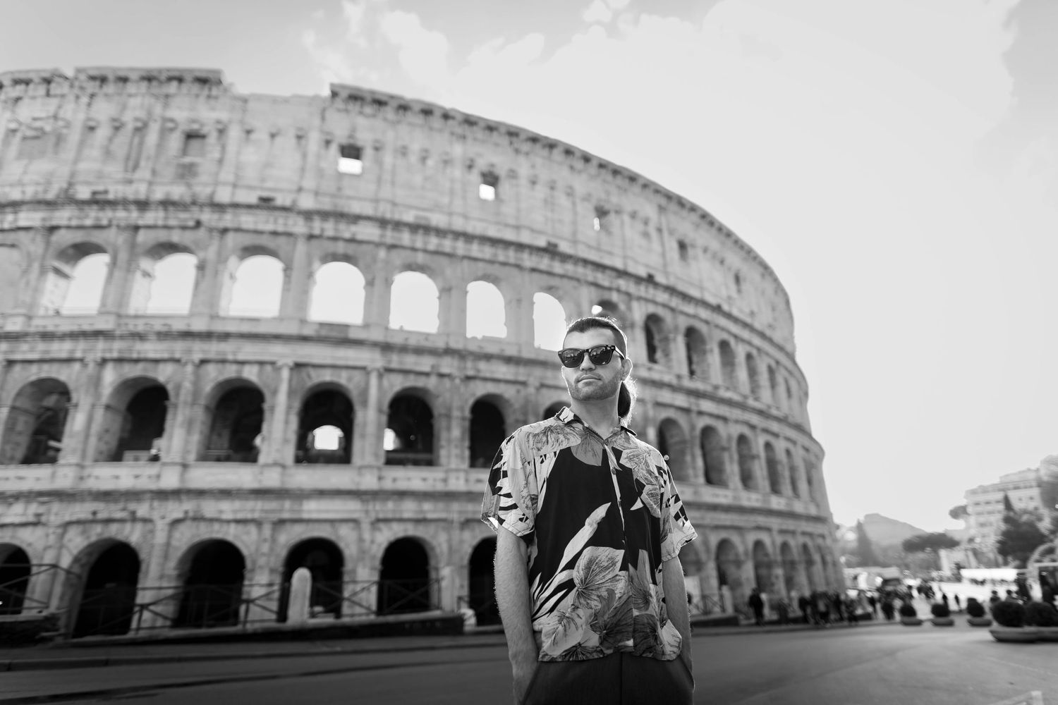 Black and white photo of a man in sunglasses posing in front of the Colosseum in Rome, Italy.