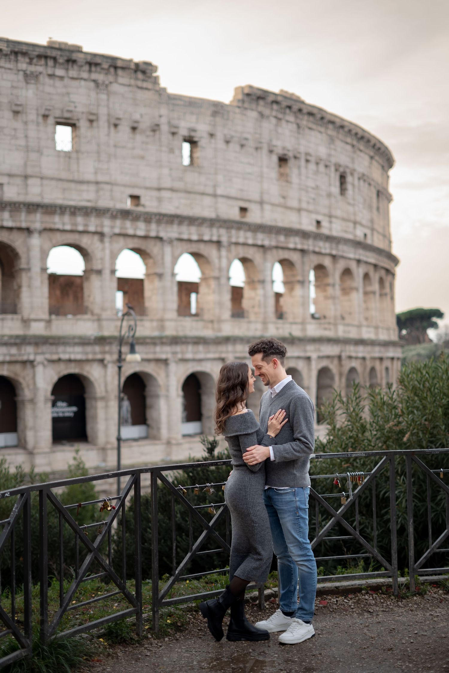 Romantic couple embracing in front of the Colosseum in Rome, Italy on a cloudy day.
