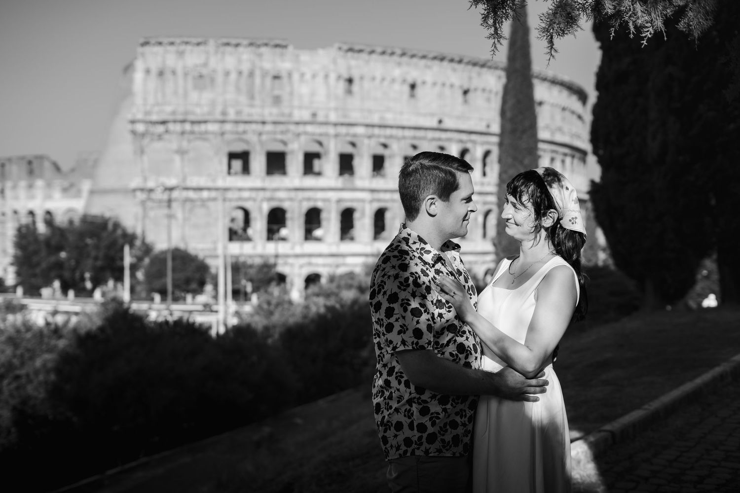 Black and white photo of a couple embracing romantically in front of the Colosseum in Rome, Italy.