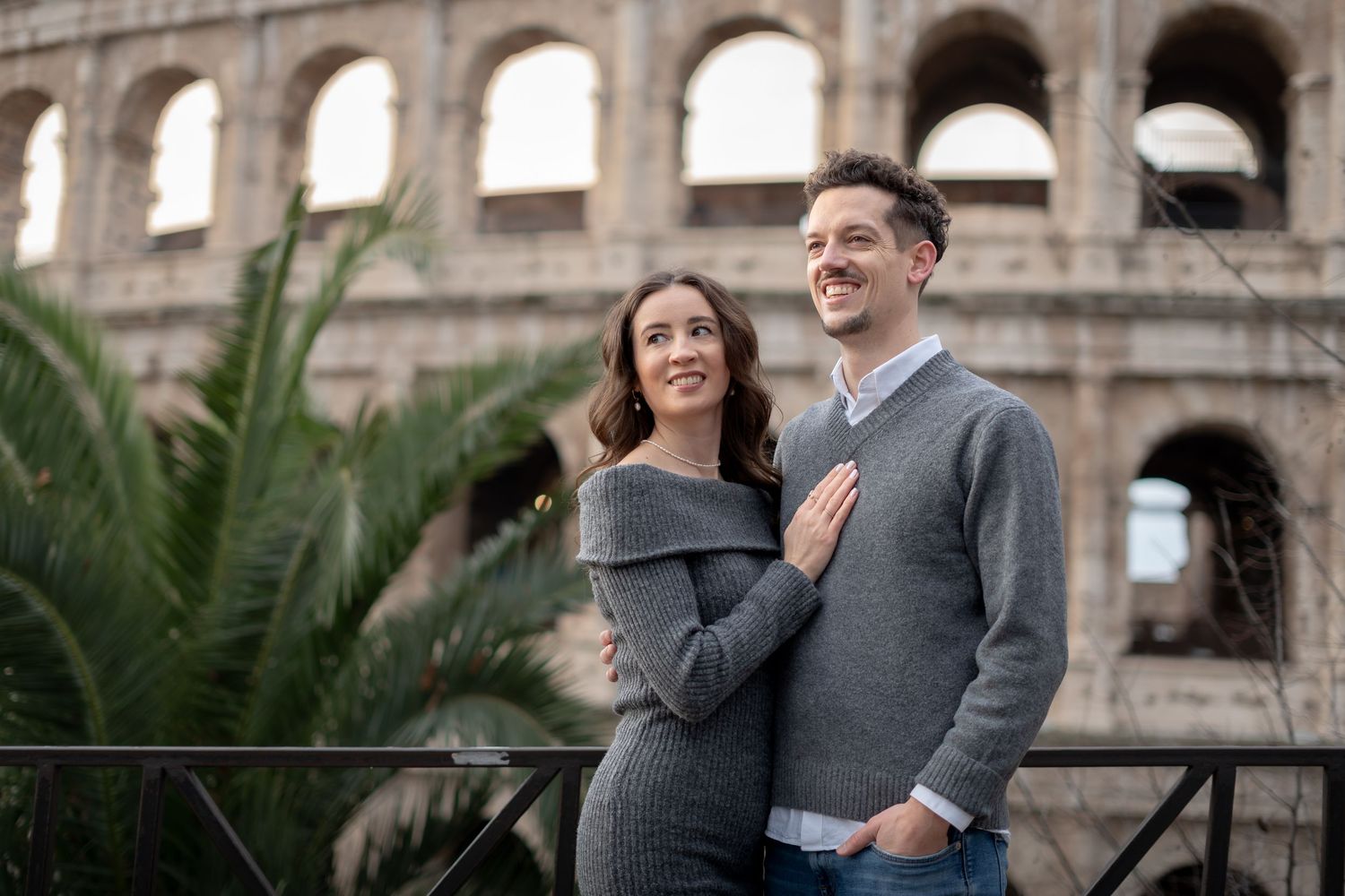 Couple posing romantically in front of the Colosseum in Rome, Italy, wearing matching gray outfits.