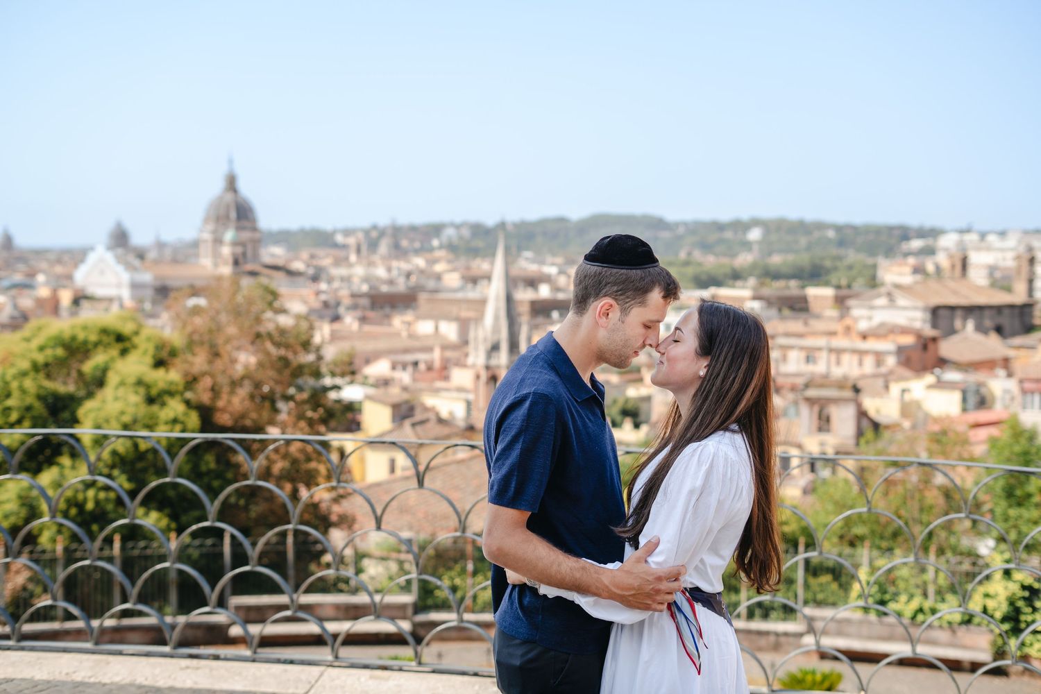 Couple sharing a romantic moment with Rome's iconic skyline and rooftops in the background on a sunny day.