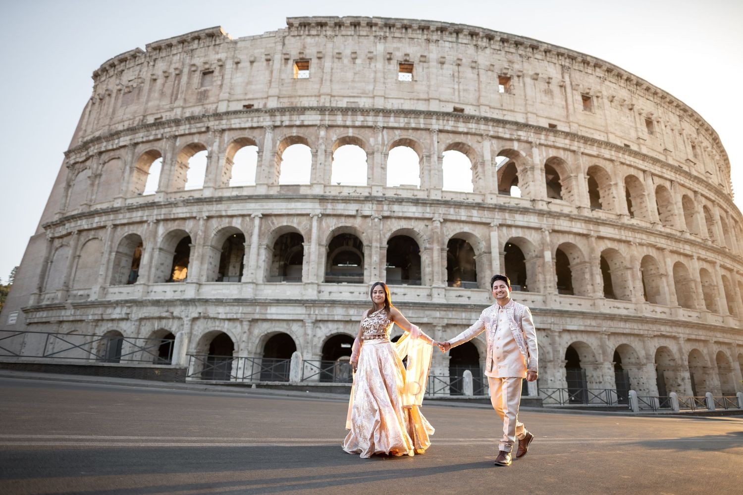 Couple in traditional attire holding hands in front of the Colosseum in Rome, Italy.