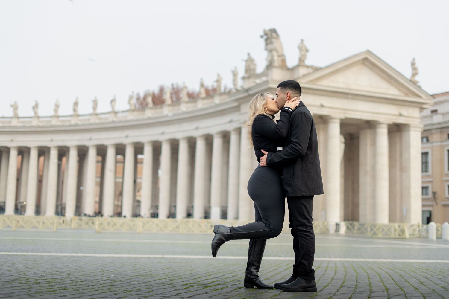 Couple embracing romantically in black outfits at St. Peter's Square, Vatican City, Rome.