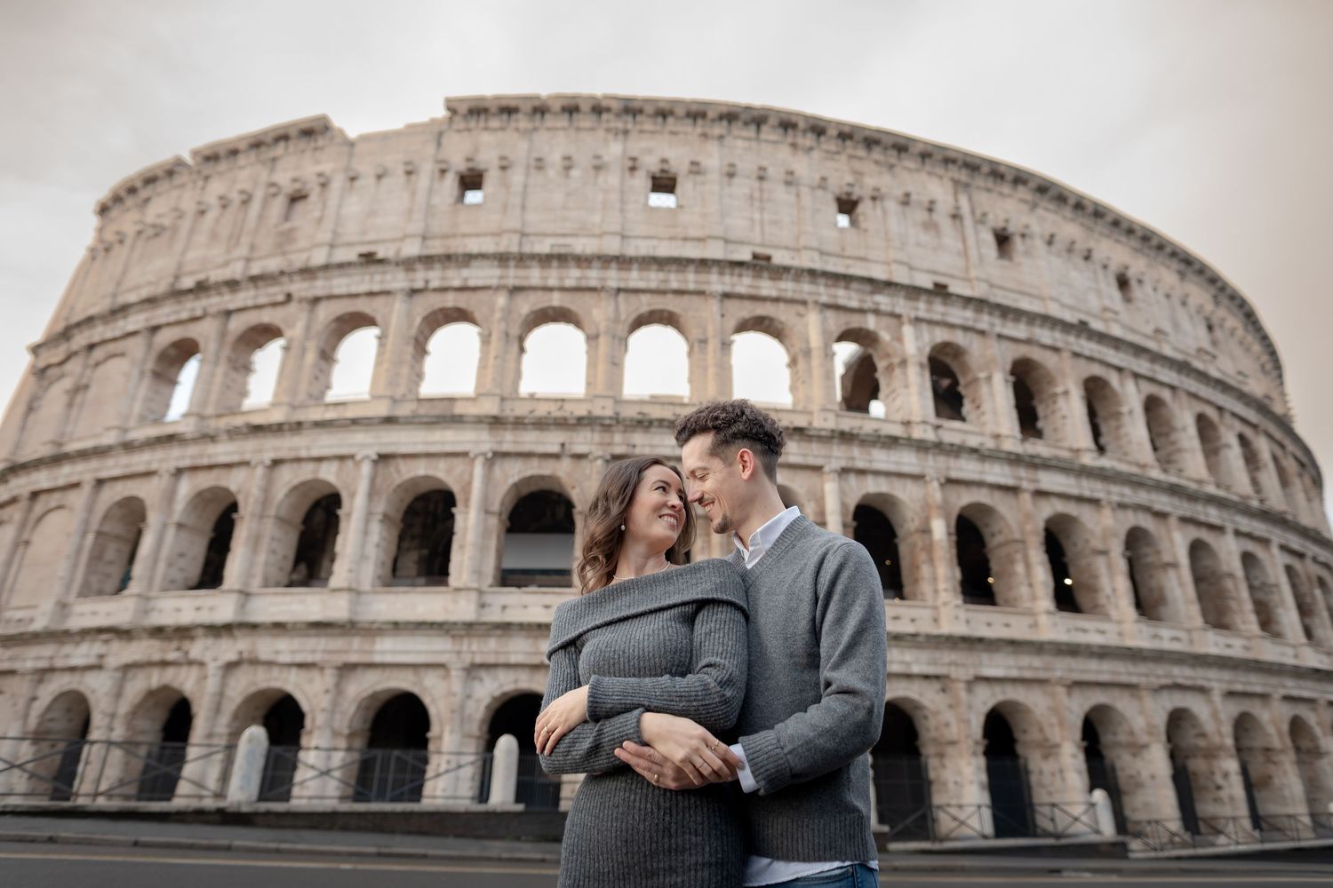 Couple embracing in front of the Colosseum in Rome, Italy, with the ancient amphitheater as a backdrop.