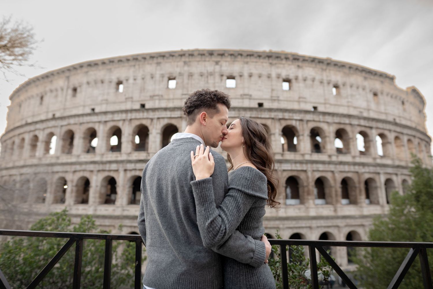 Couple sharing a romantic kiss in front of the ancient Colosseum in Rome, Italy.