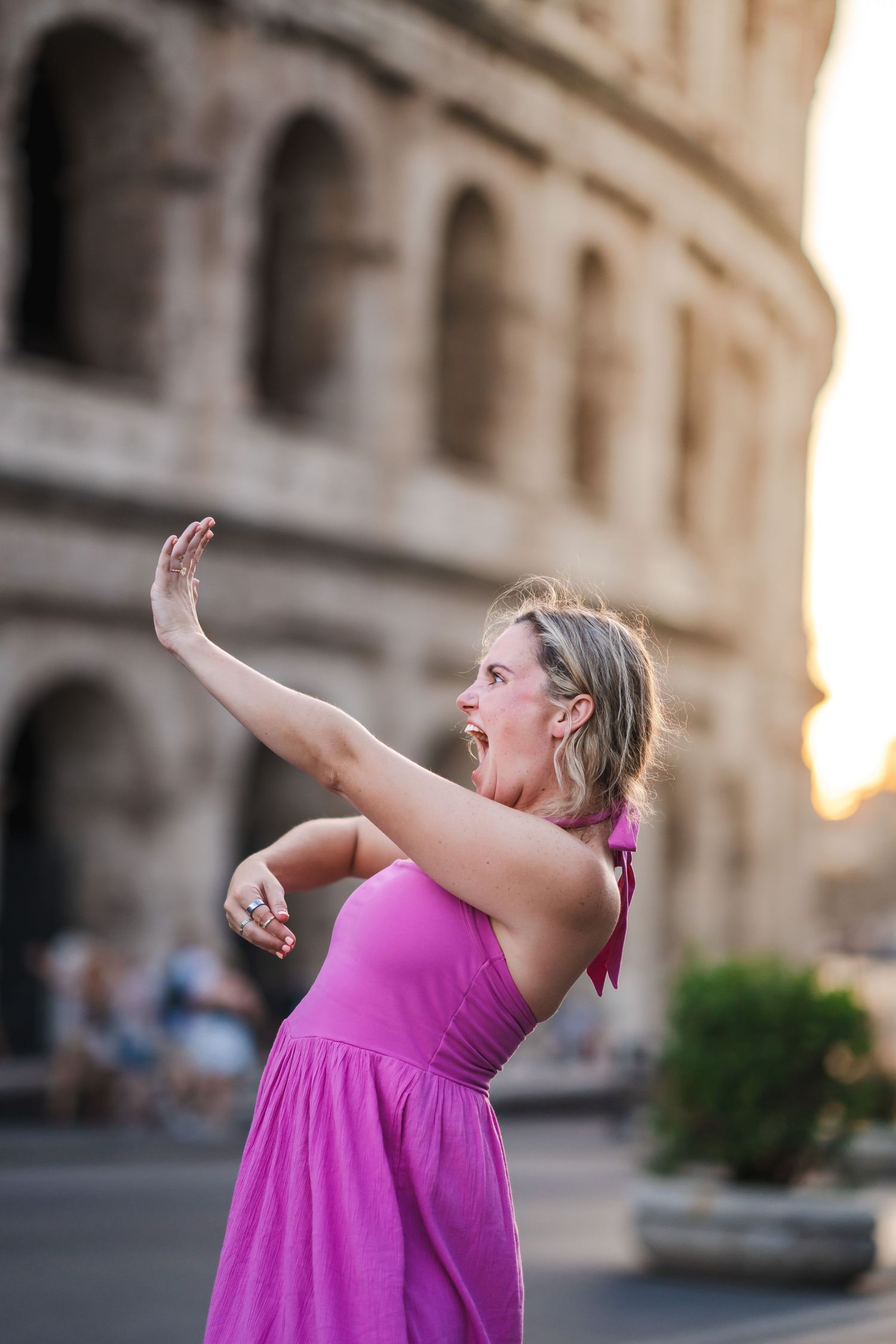 Woman in pink dress posing expressively in front of the Colosseum in Rome at sunset.