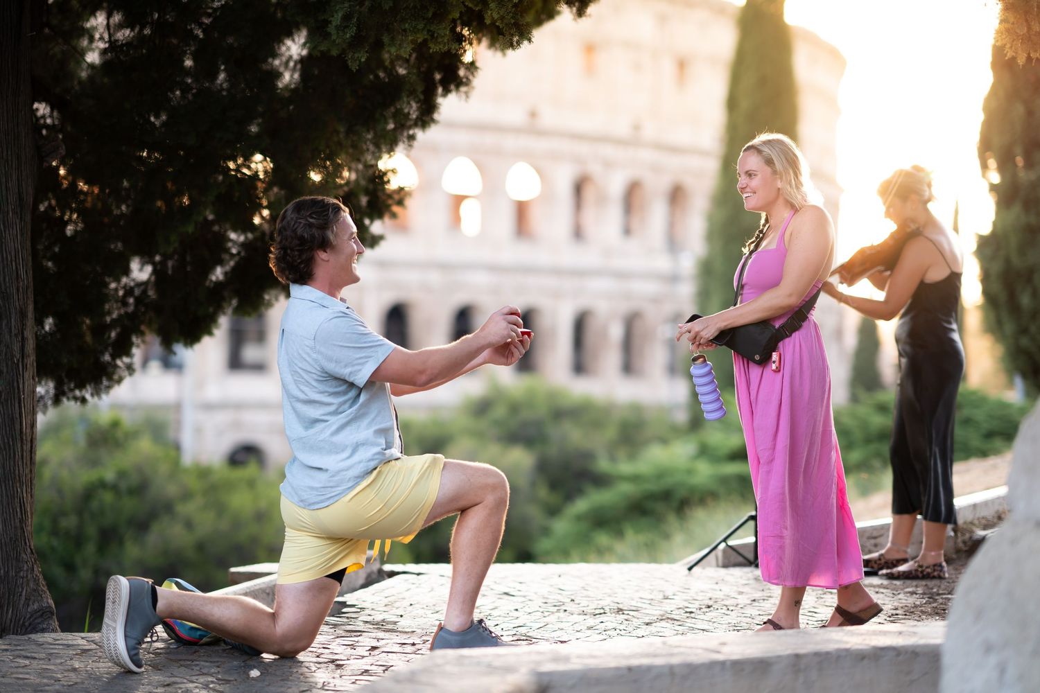 Man proposes to woman on one knee near the Colosseum in Rome at sunset.