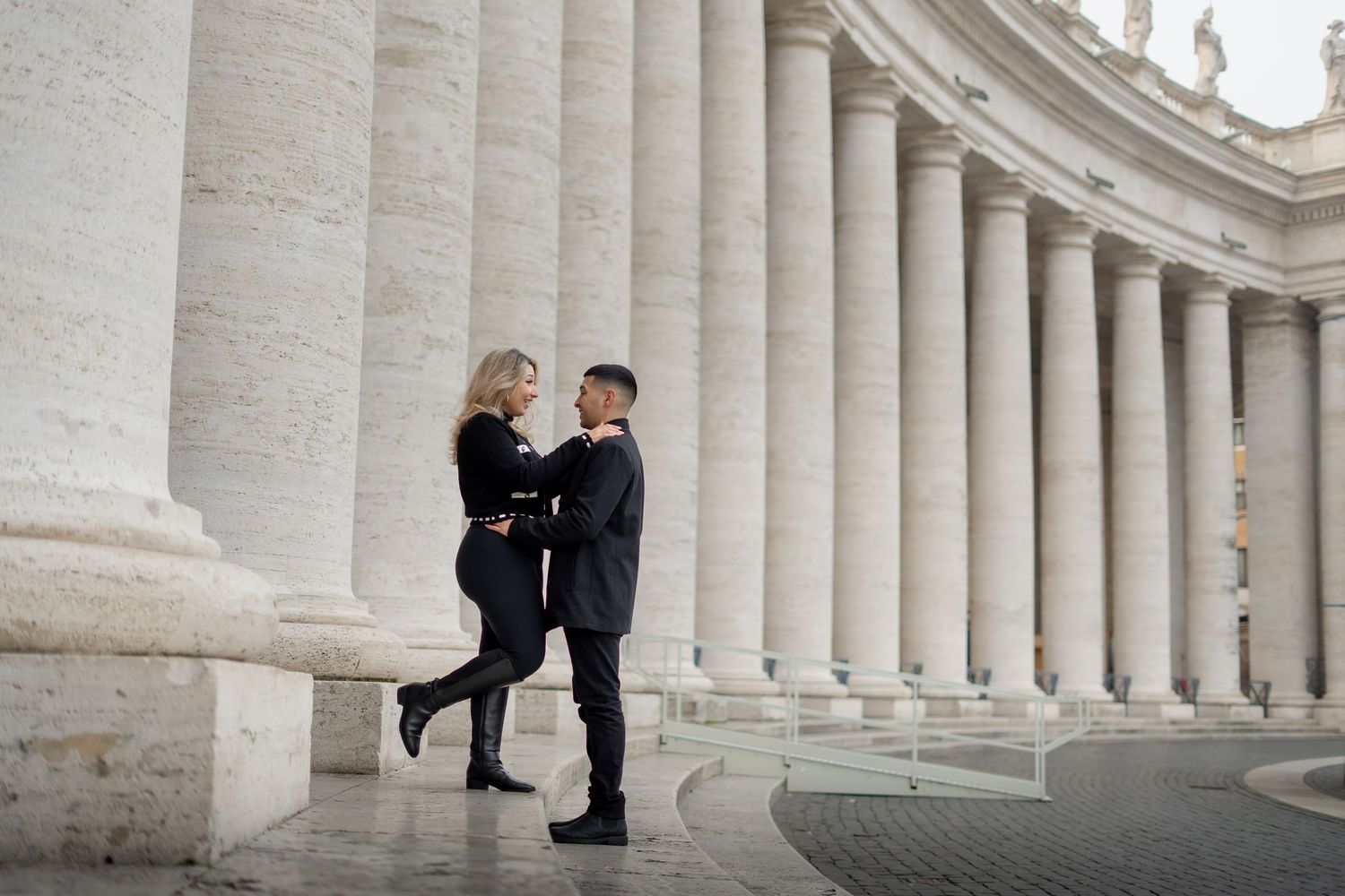 Couple embracing romantically among grand marble columns at St. Peter's Square, Vatican City, Rome.