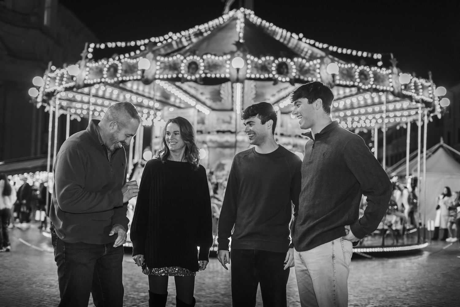 Black and white photo of a family of four standing near a lit carousel at night in Rome.