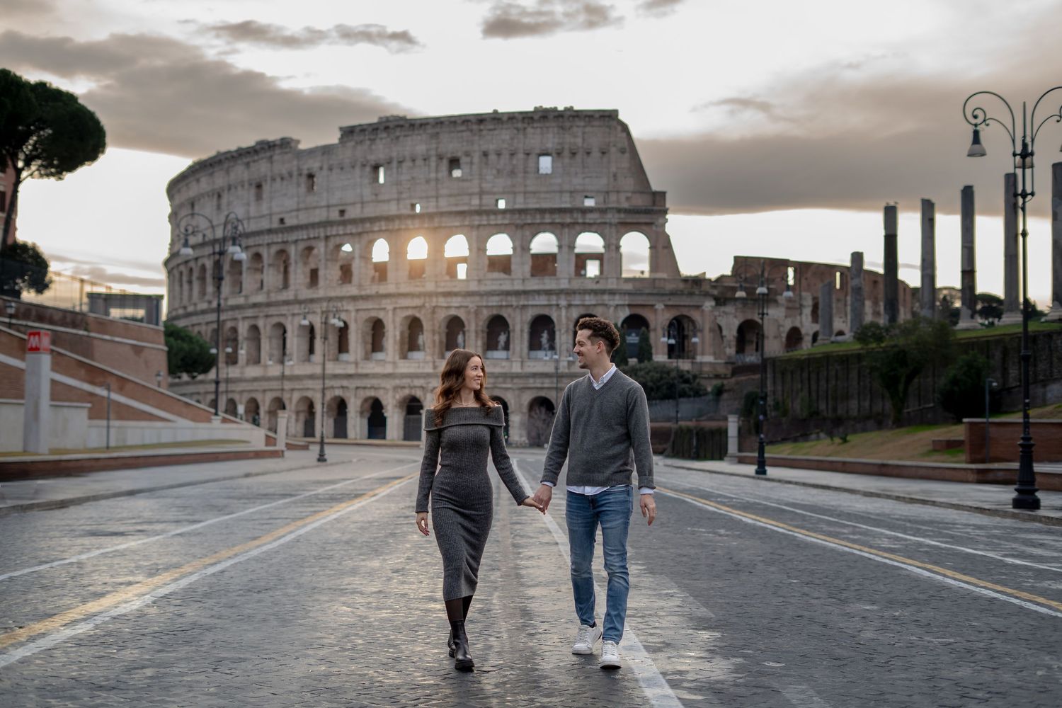 Couple holding hands walking in front of the Colosseum in Rome, Italy at dusk.