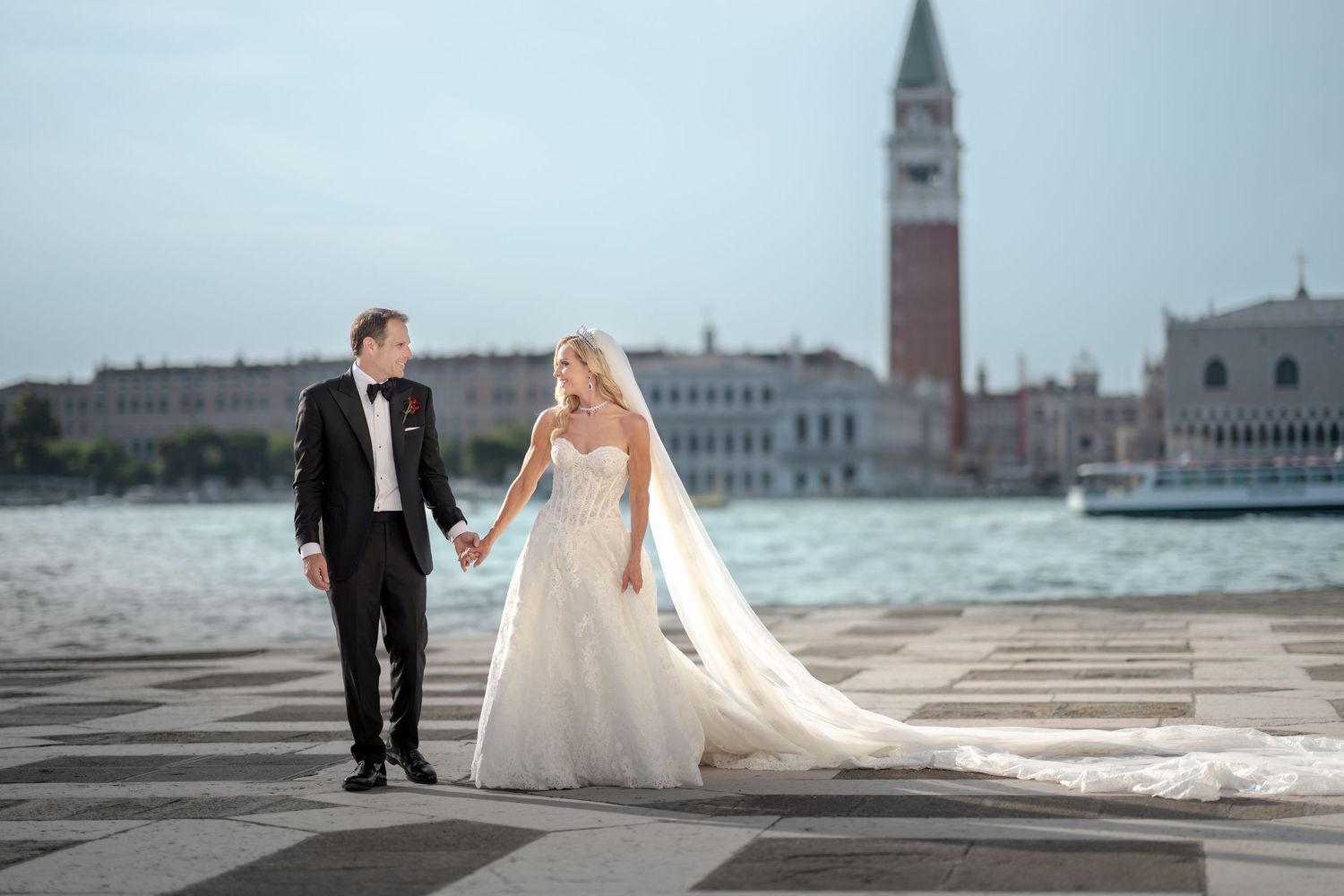 Bride and groom holding hands at Venice waterfront with Campanile and Doge's Palace in background.
