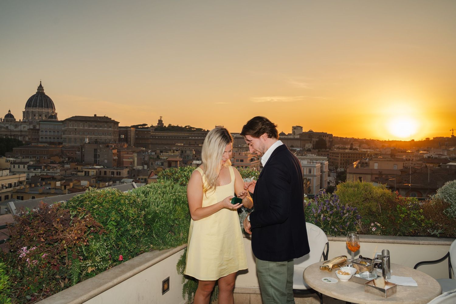 Couple enjoying drinks on a rooftop terrace with a stunning Rome sunset skyline view.