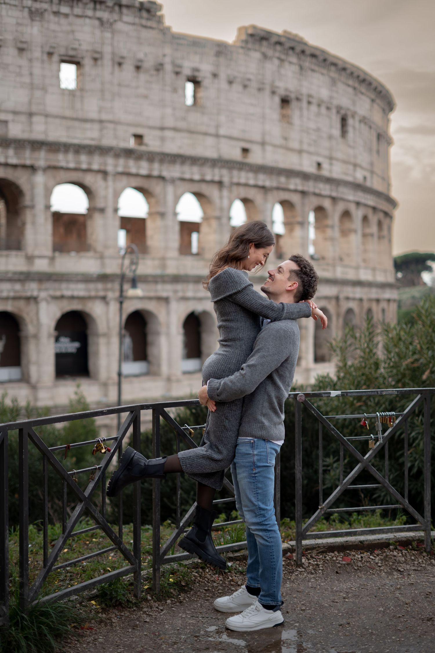 Romantic couple embracing in front of the Colosseum in Rome, Italy, sharing a tender moment outdoors.