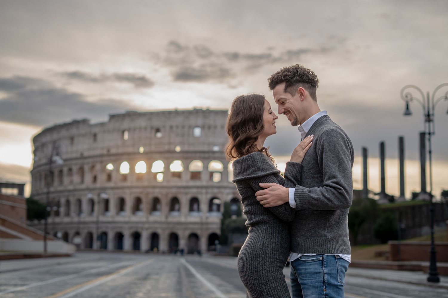 Romantic couple embracing in front of the Colosseum at sunrise in Rome, Italy.