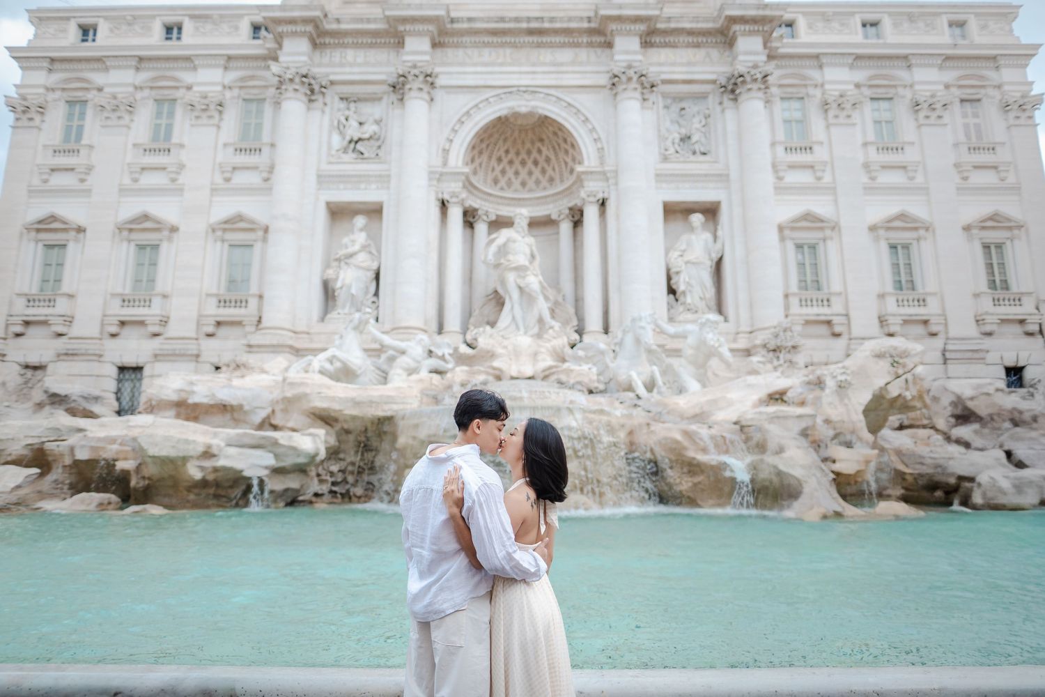 Couple kissing in front of the Trevi Fountain in Rome, Italy, with turquoise water and baroque sculptures.