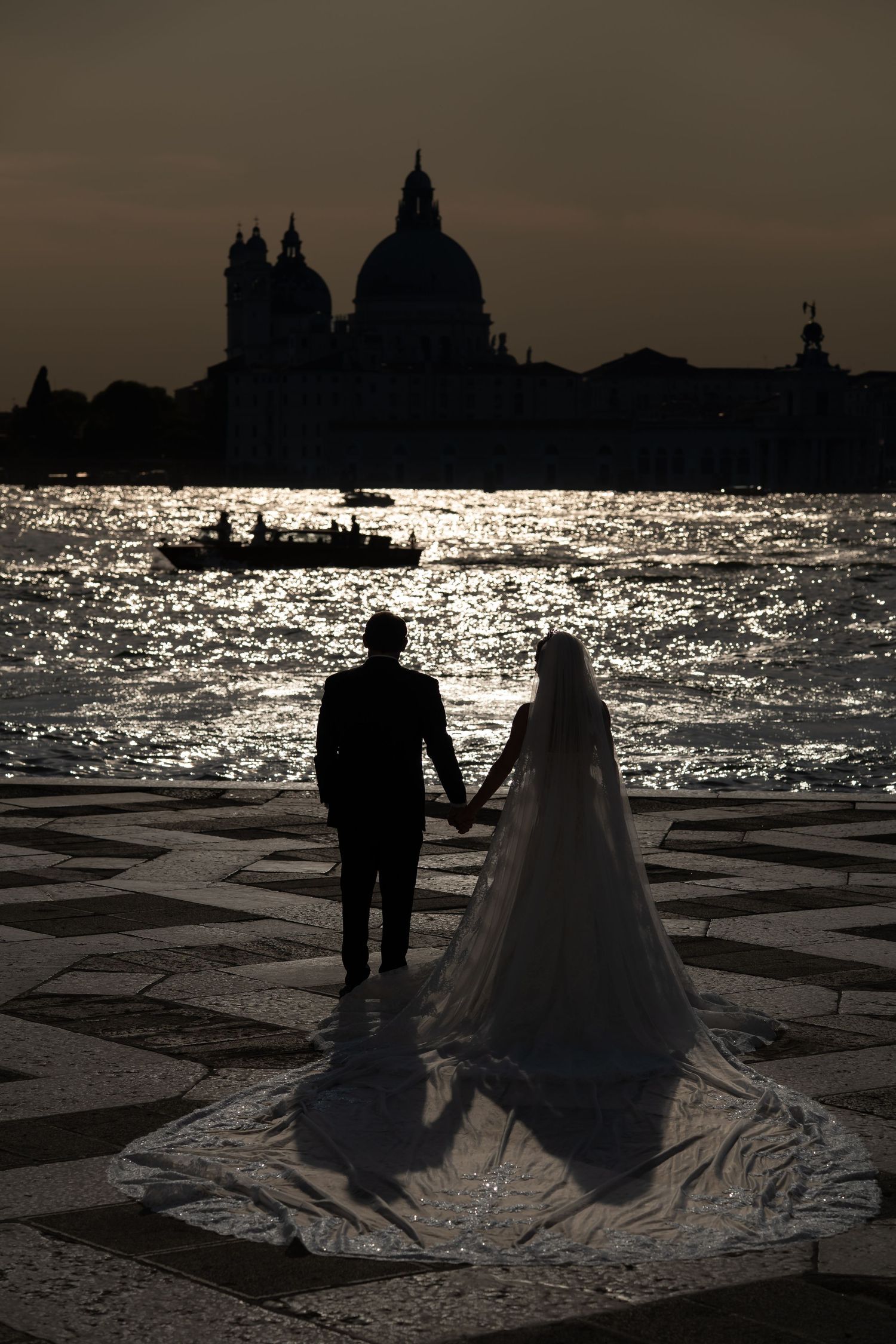 Silhouette of bride and groom holding hands at sunset in Venice, with Santa Maria della Salute basilica in background.