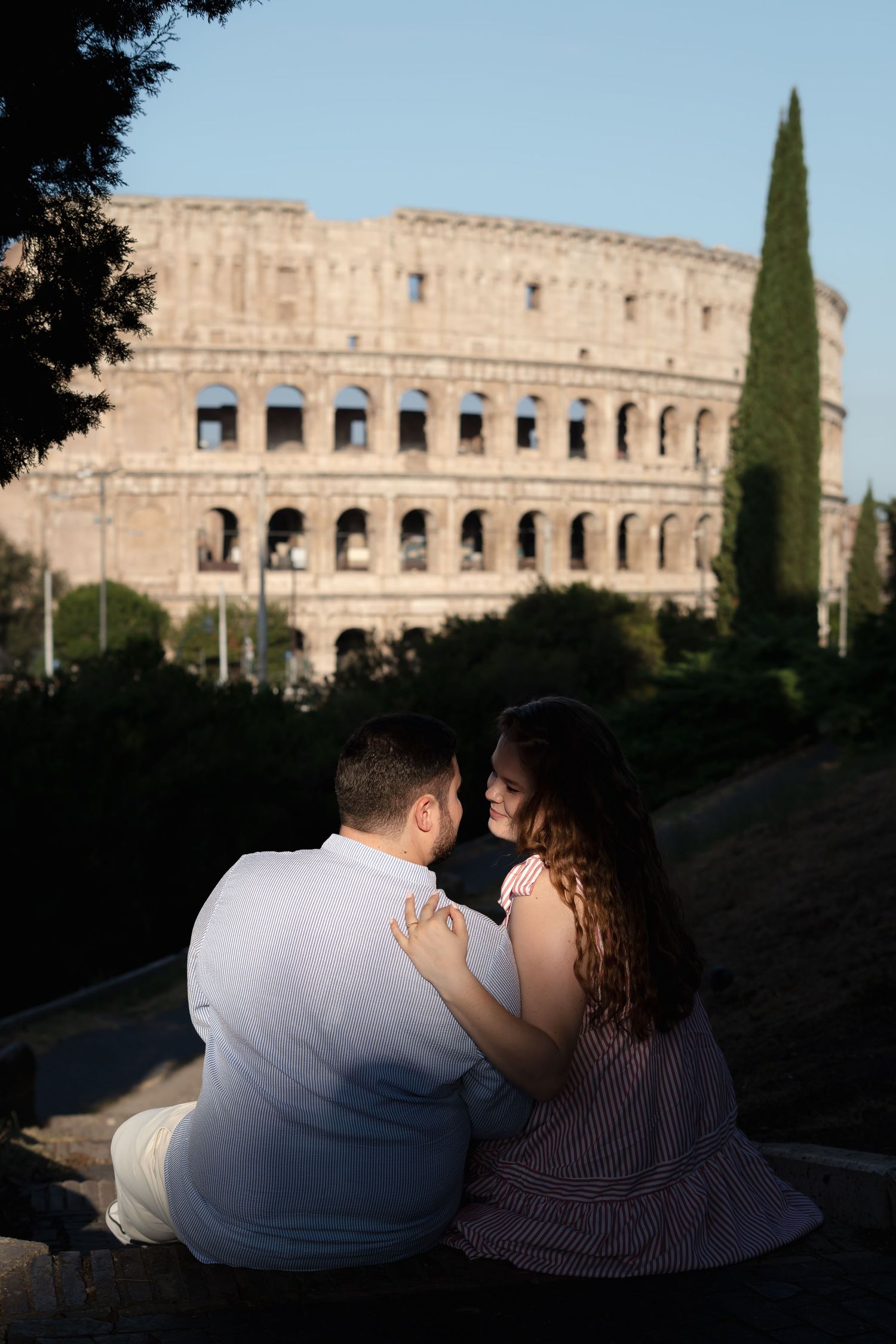 Couple sitting together in front of the Colosseum in Rome, Italy, on a sunny day.