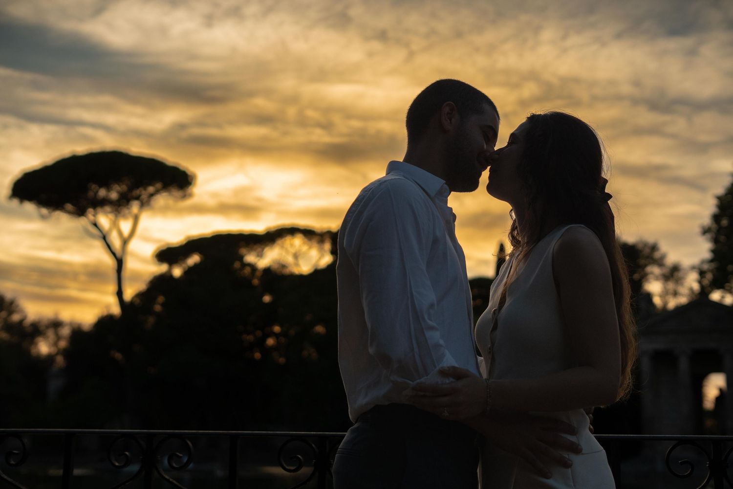 Romantic silhouette of a couple sharing an intimate moment at sunset with dramatic golden sky backdrop.