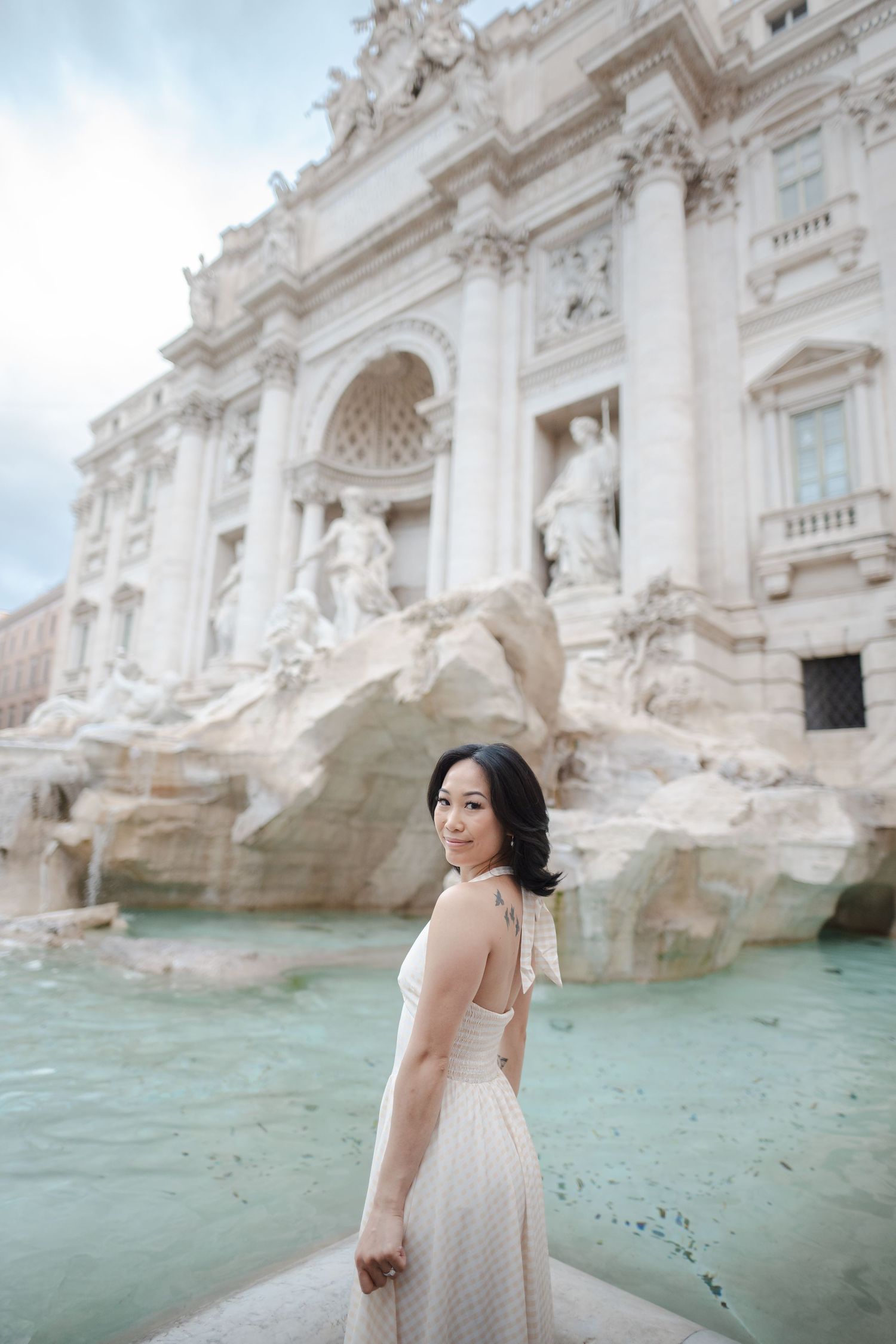 Woman in elegant dress posing at Trevi Fountain Rome.