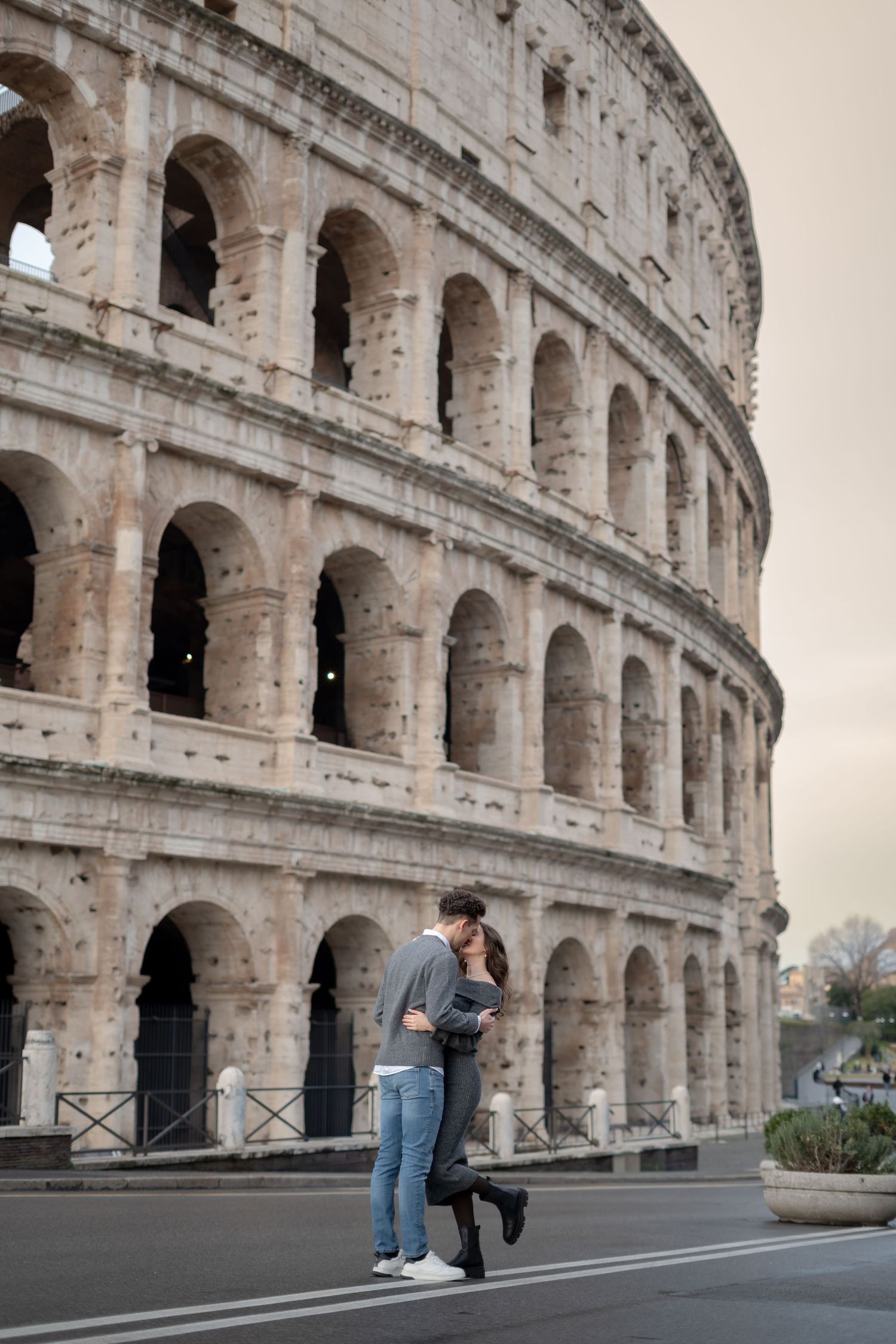 Romantic couple kissing in front of the ancient Colosseum in Rome, Italy, on a quiet street.