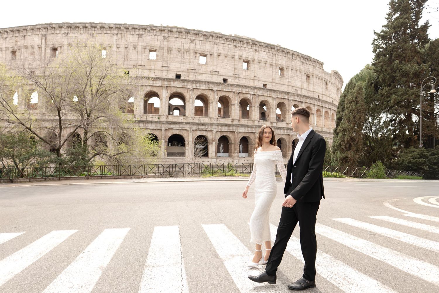 Couple in wedding attire crossing a zebra crossing in front of the Colosseum in Rome, Italy.