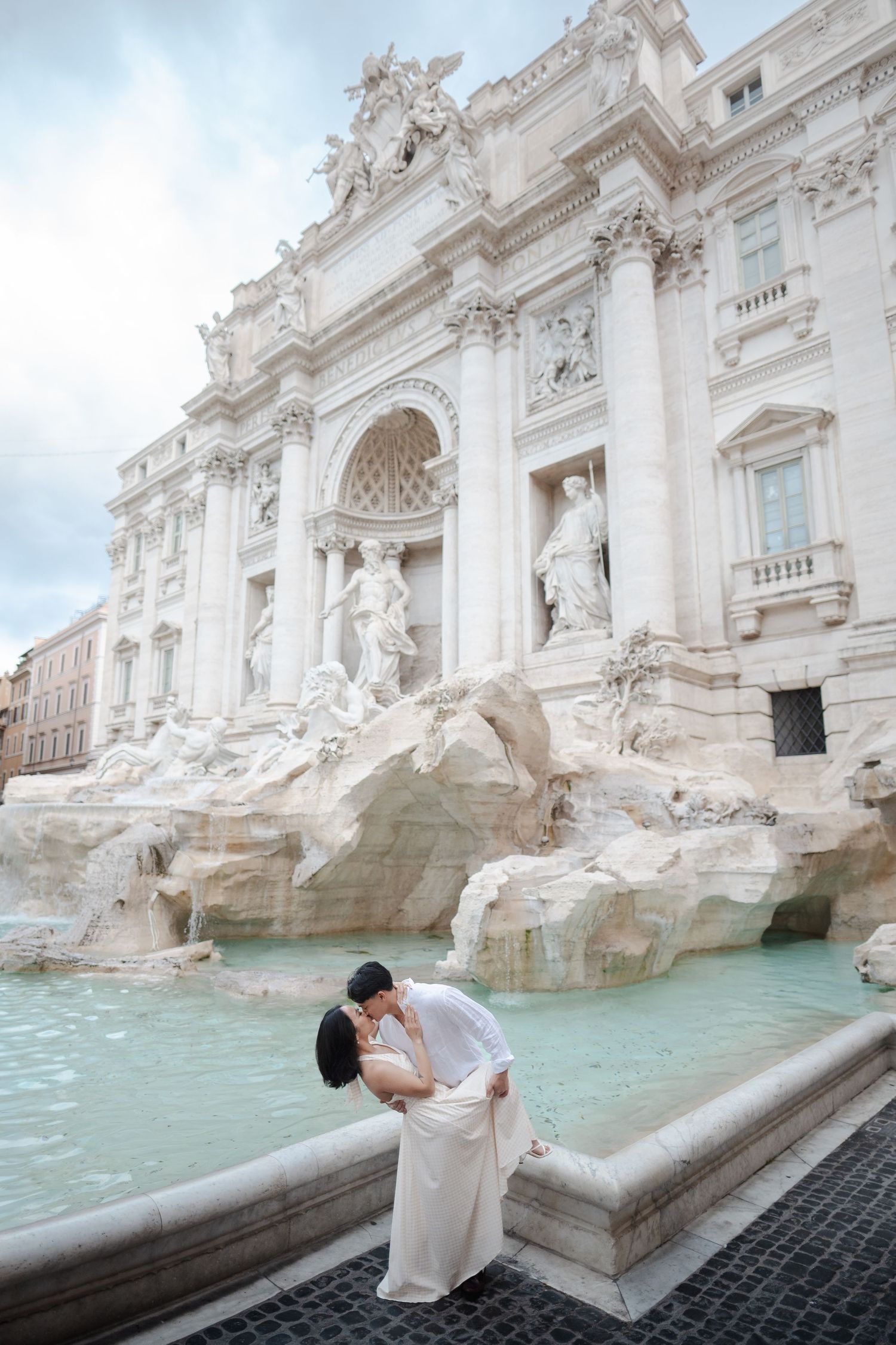 Couple sharing a romantic dip kiss in front of the iconic Trevi Fountain in Rome.