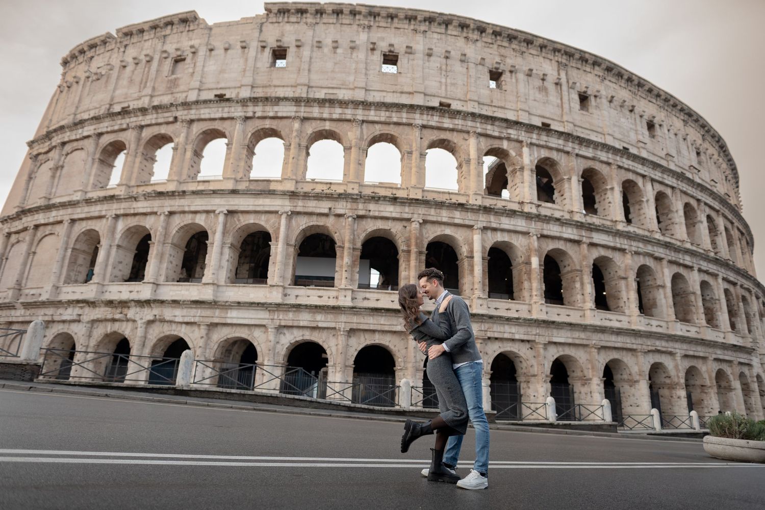 Couple embracing in front of the ancient Colosseum in Rome, Italy, on a cloudy day.