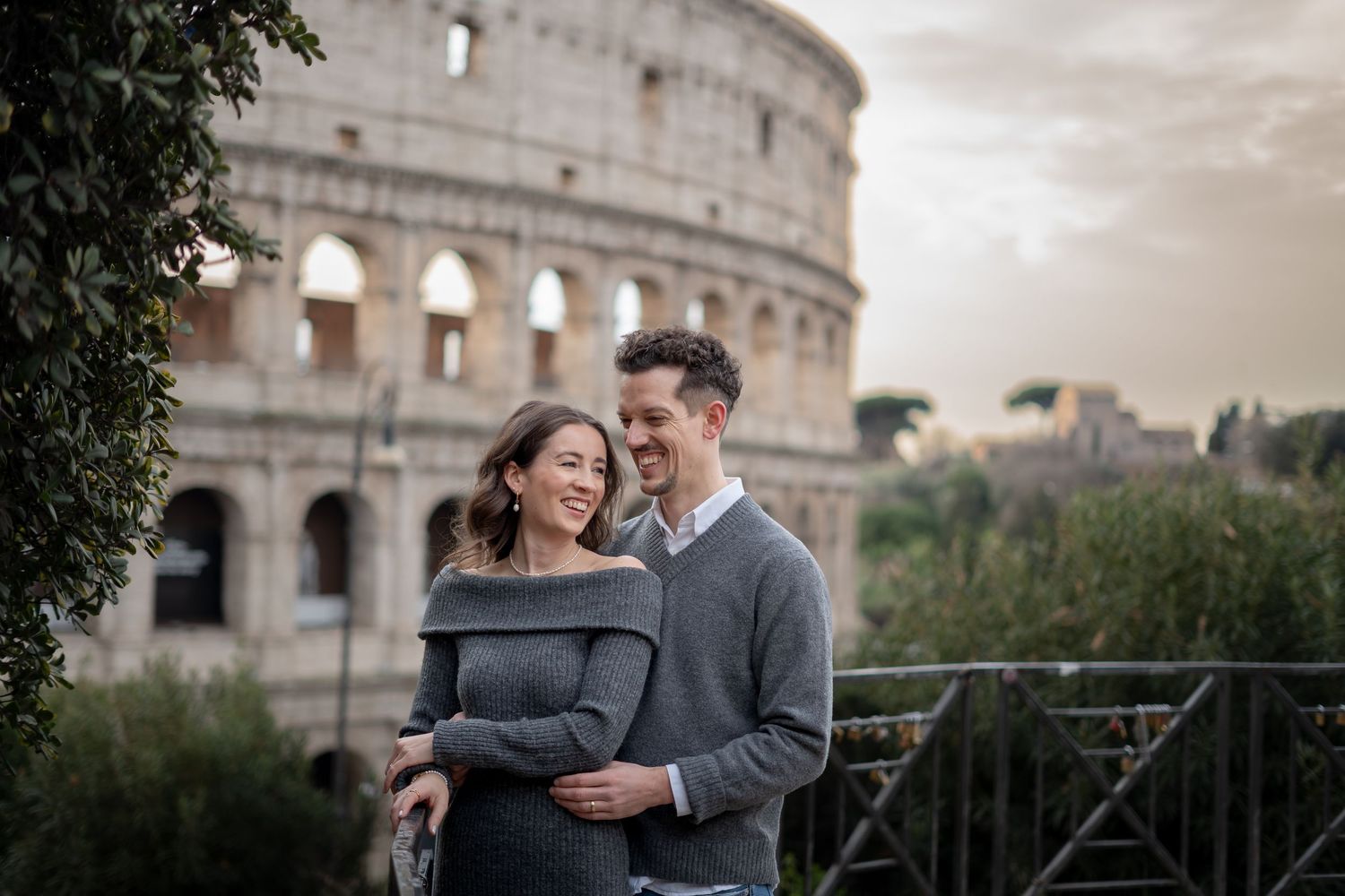 Couple embracing and smiling in front of the Colosseum in Rome, Italy at sunset.