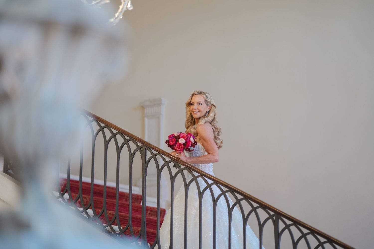 Elegant bride descending grand staircase holding vibrant pink bouquet in a classic Italian venue.