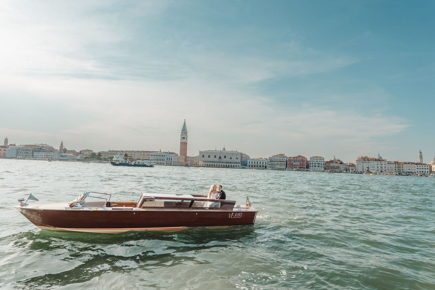 A classic wooden water taxi glides across the Venice lagoon with St. Marks Campanile in the background.