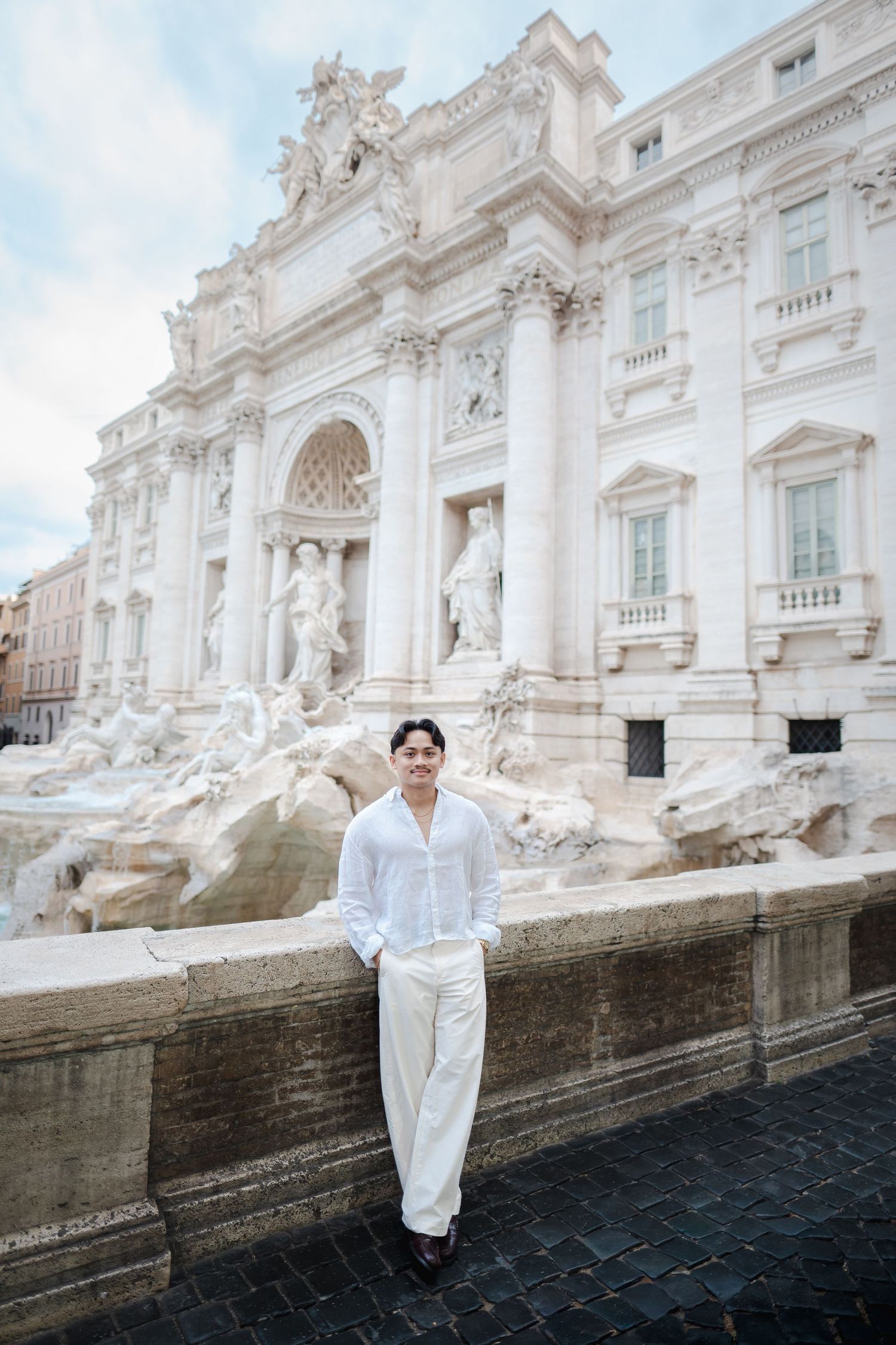 Man in white outfit posing at Trevi Fountain Rome.