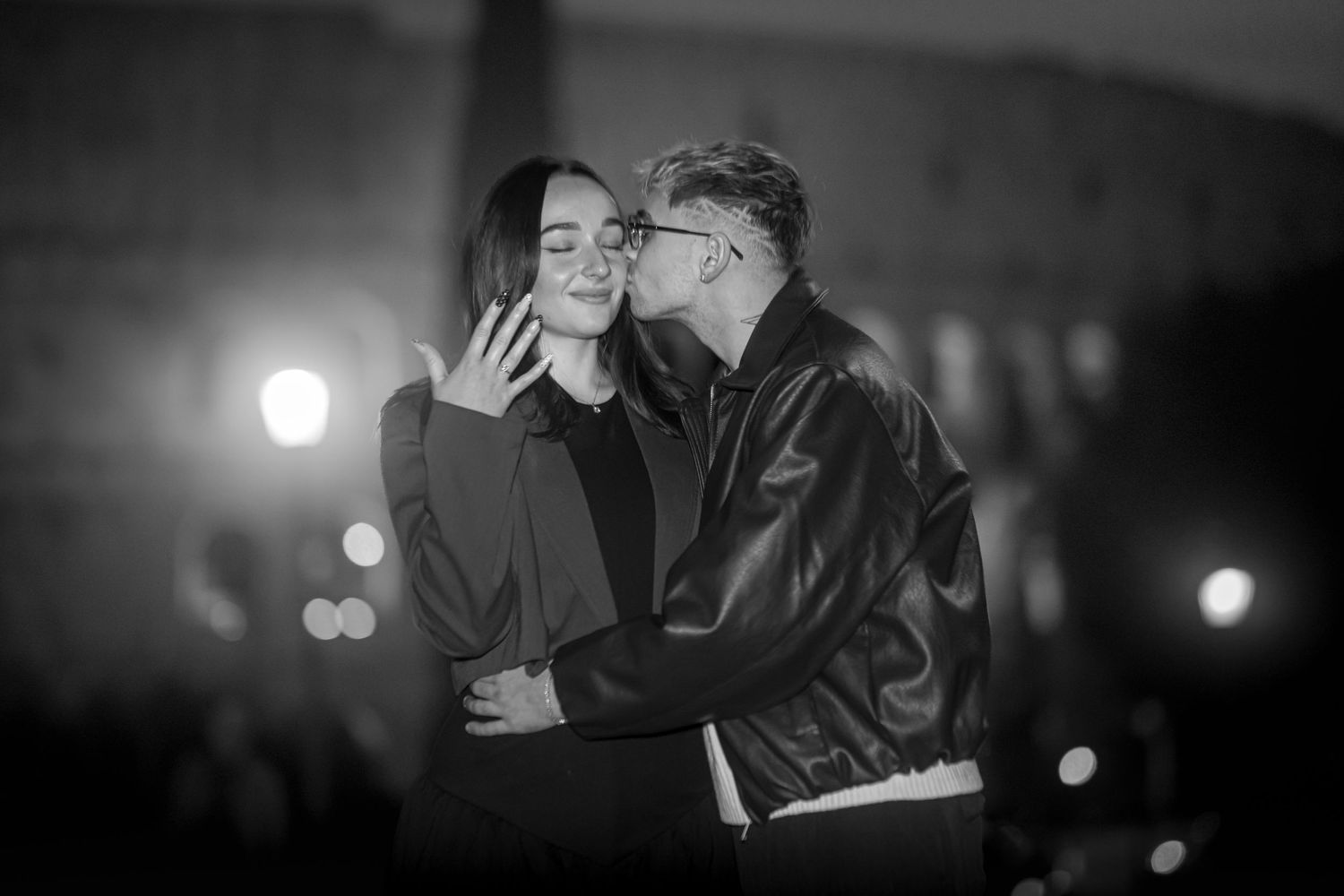 Black and white photo of a couple sharing a tender kiss at night in Rome, Italy.