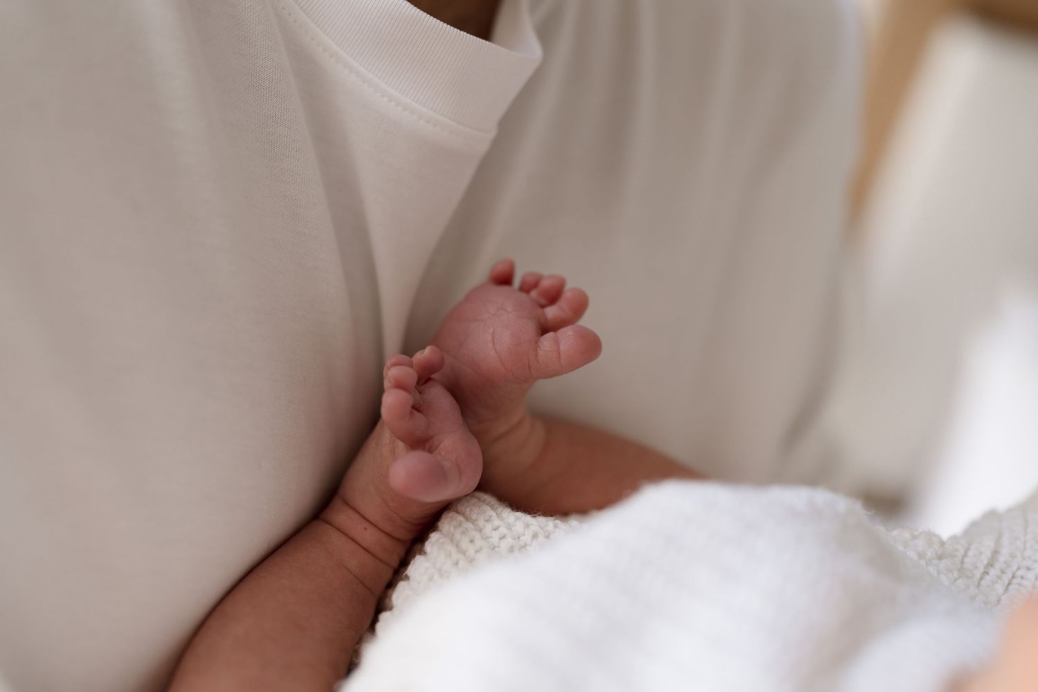 Close up view of tiny newborn baby hands resting on soft white blanket.