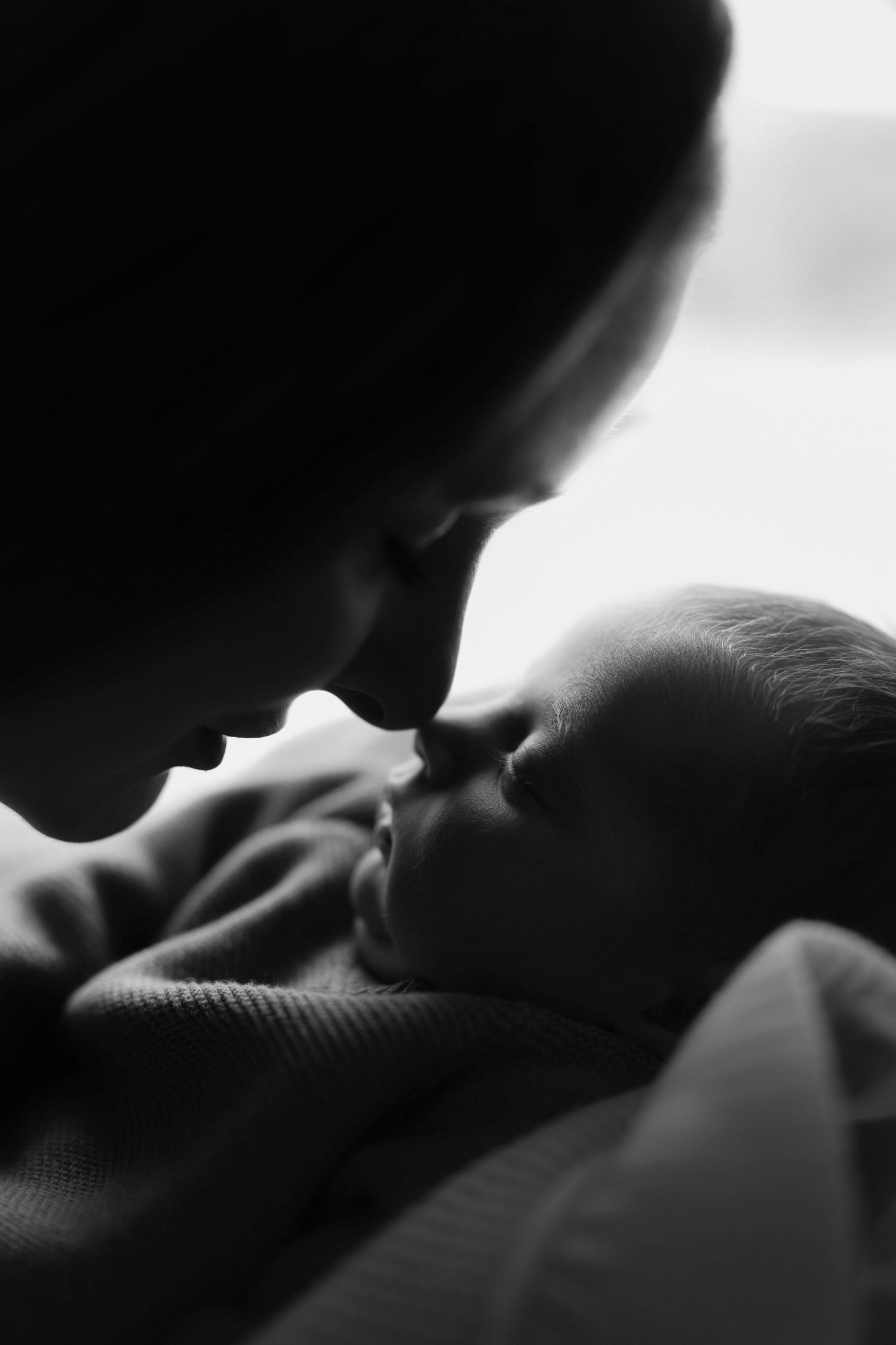 Black and white photo of a mother tenderly touching noses with her sleeping newborn baby.