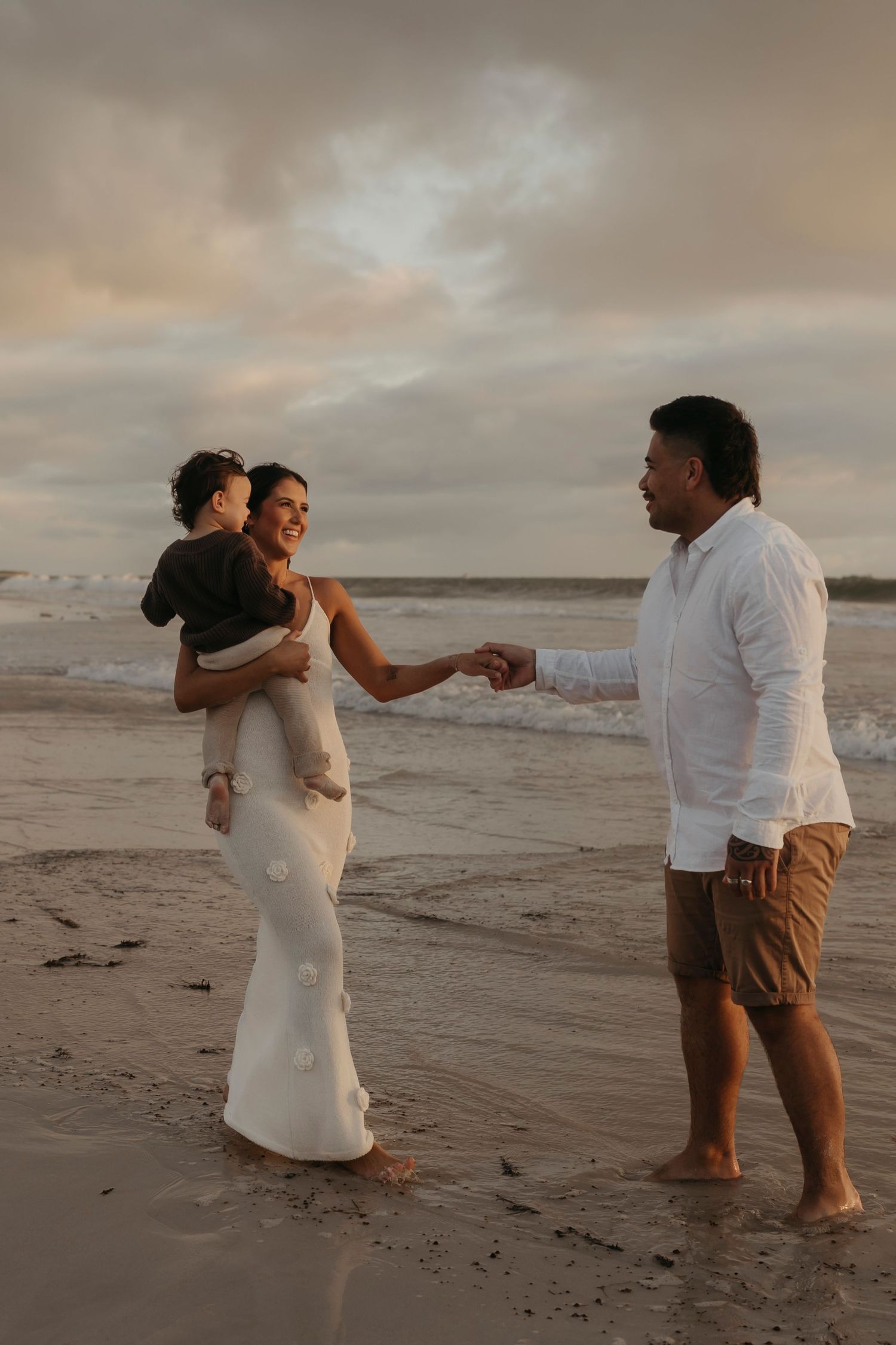 A couple holding a child sharing an intimate moment together on a sandy beach at dusk.