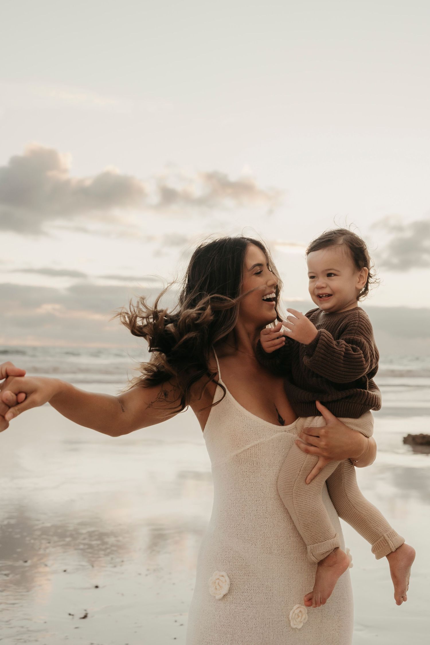 A joyful moment captured at sunset on the beach as figures dance together in a white dress against cloudy skies.