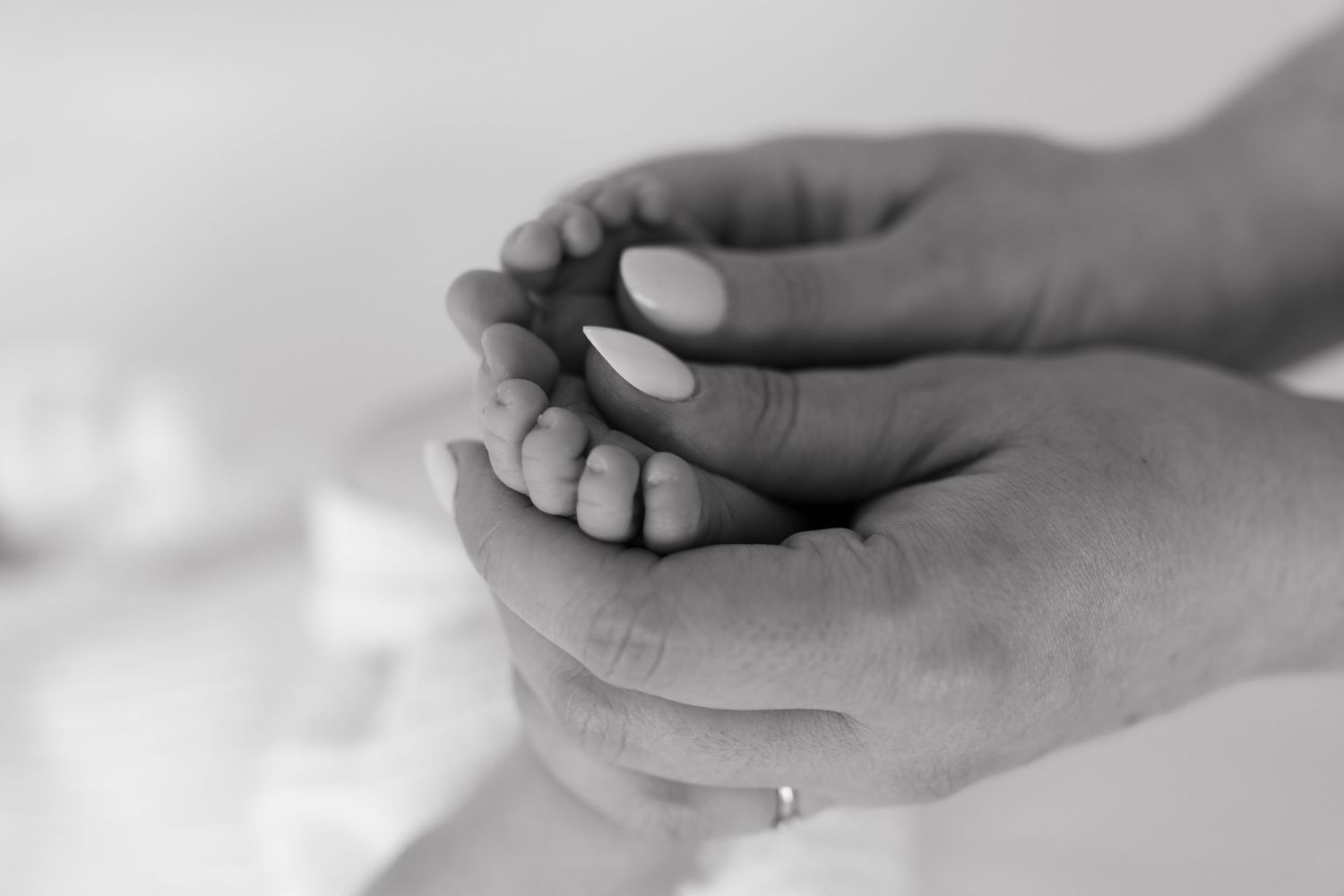 Close up black and white photo of adult hands gently holding tiny infant feet.