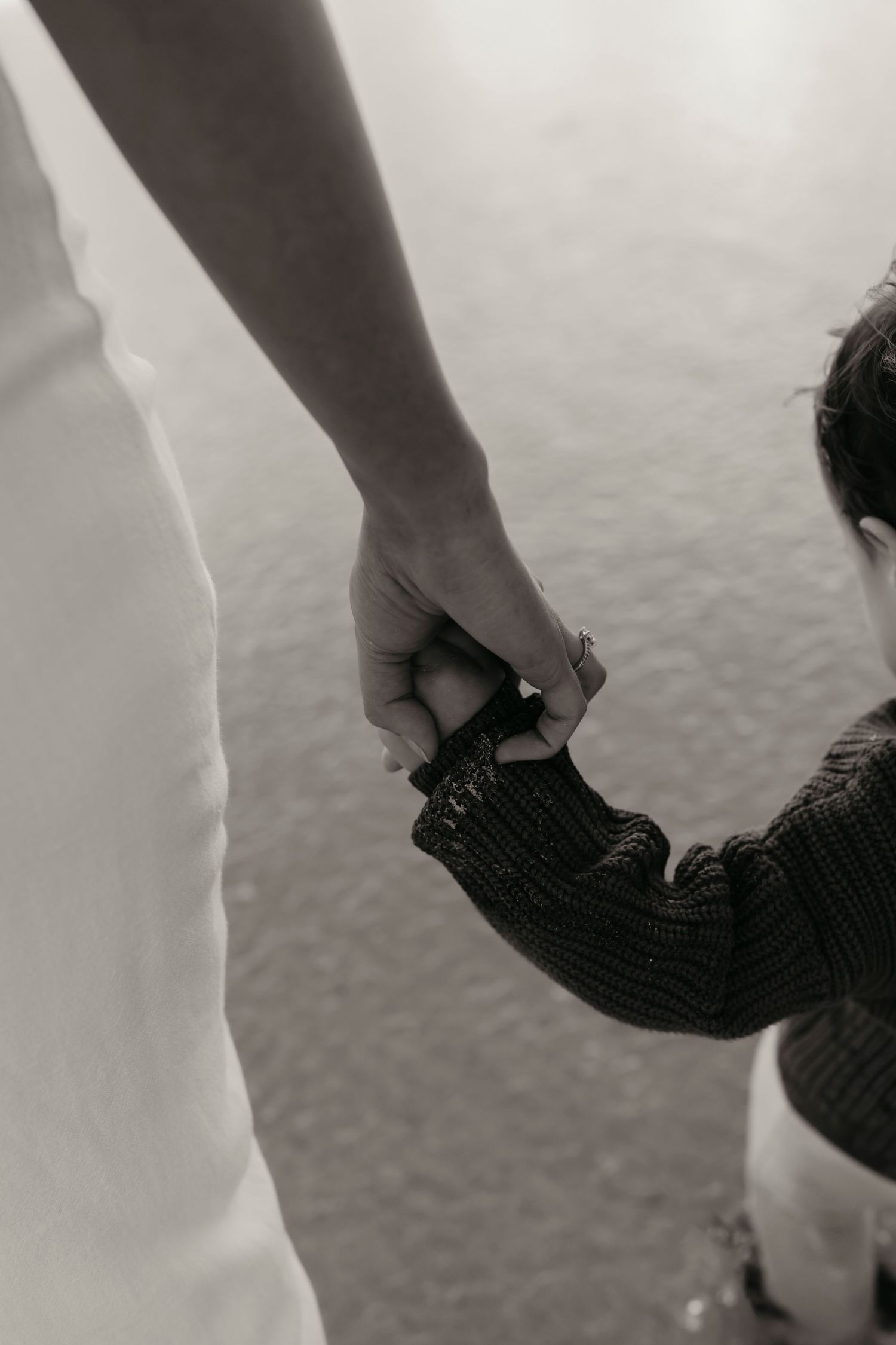 Black and white close-up photo of an adult's hand holding a child's hand wearing a knit glove.