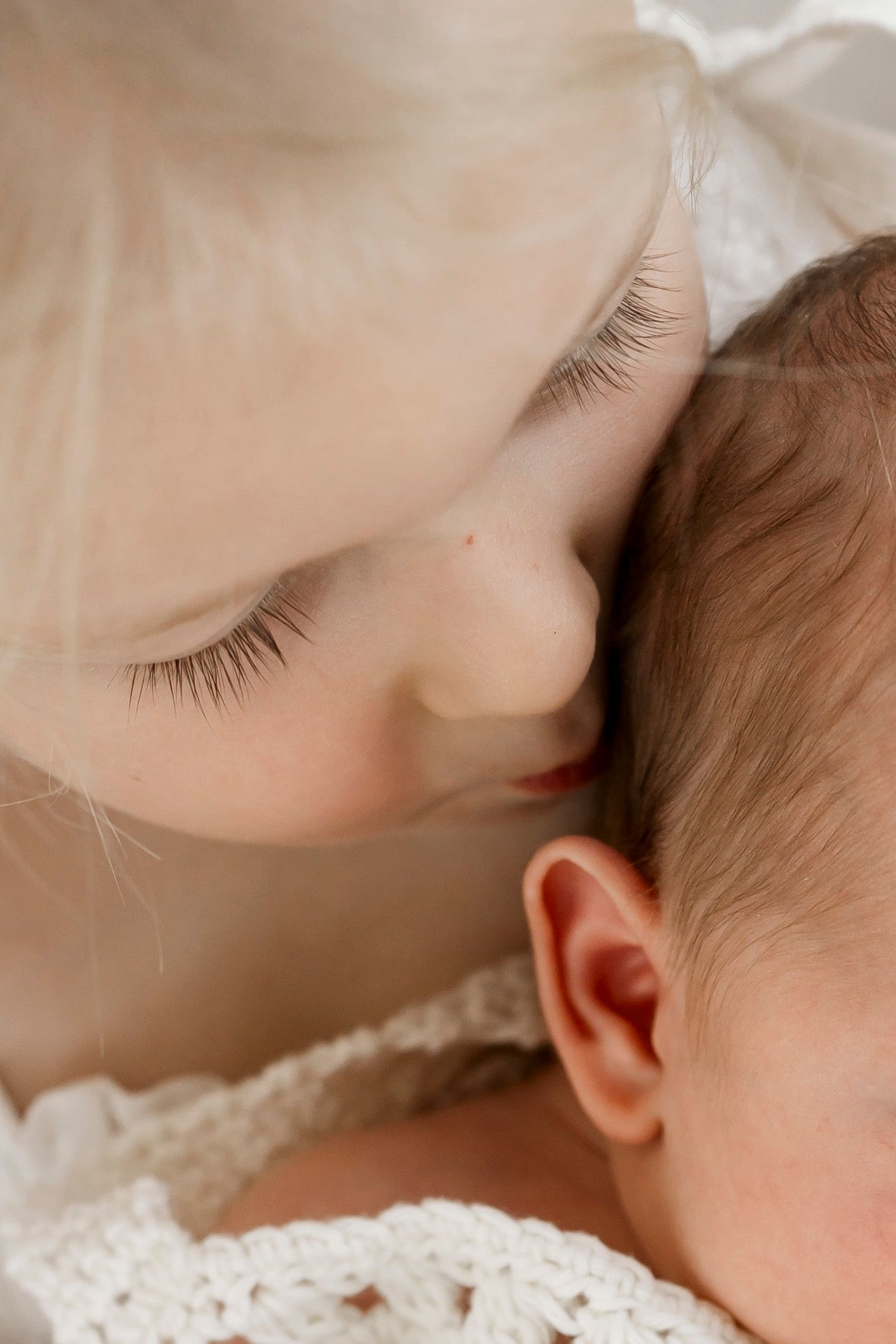 Close up macro shot of a tender moment showing a baby being gently snuggled with light skin tones and soft eyelashes.
